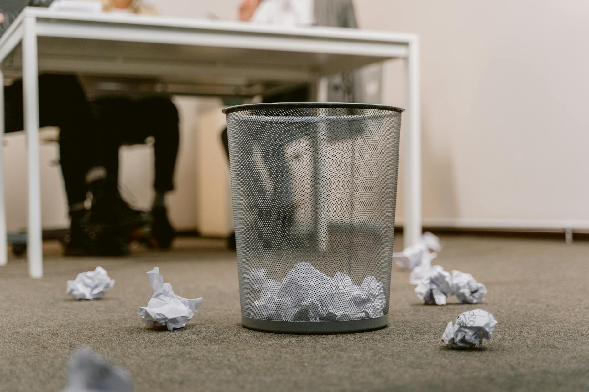 Office floor with a visible trash bin and crumpled papers scattered around, blurring human figures. - declutter communication
