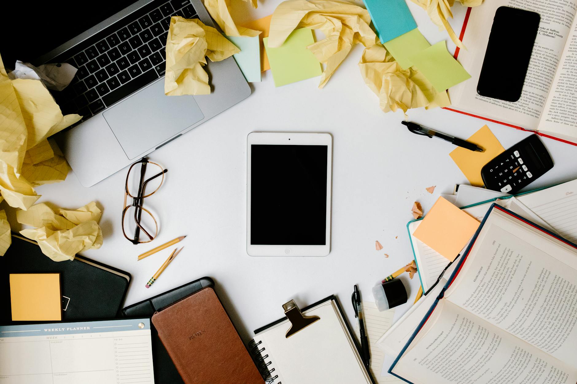 Overhead view of a cluttered workspace with gadgets, crumpled papers, and office supplies. - declutter communication