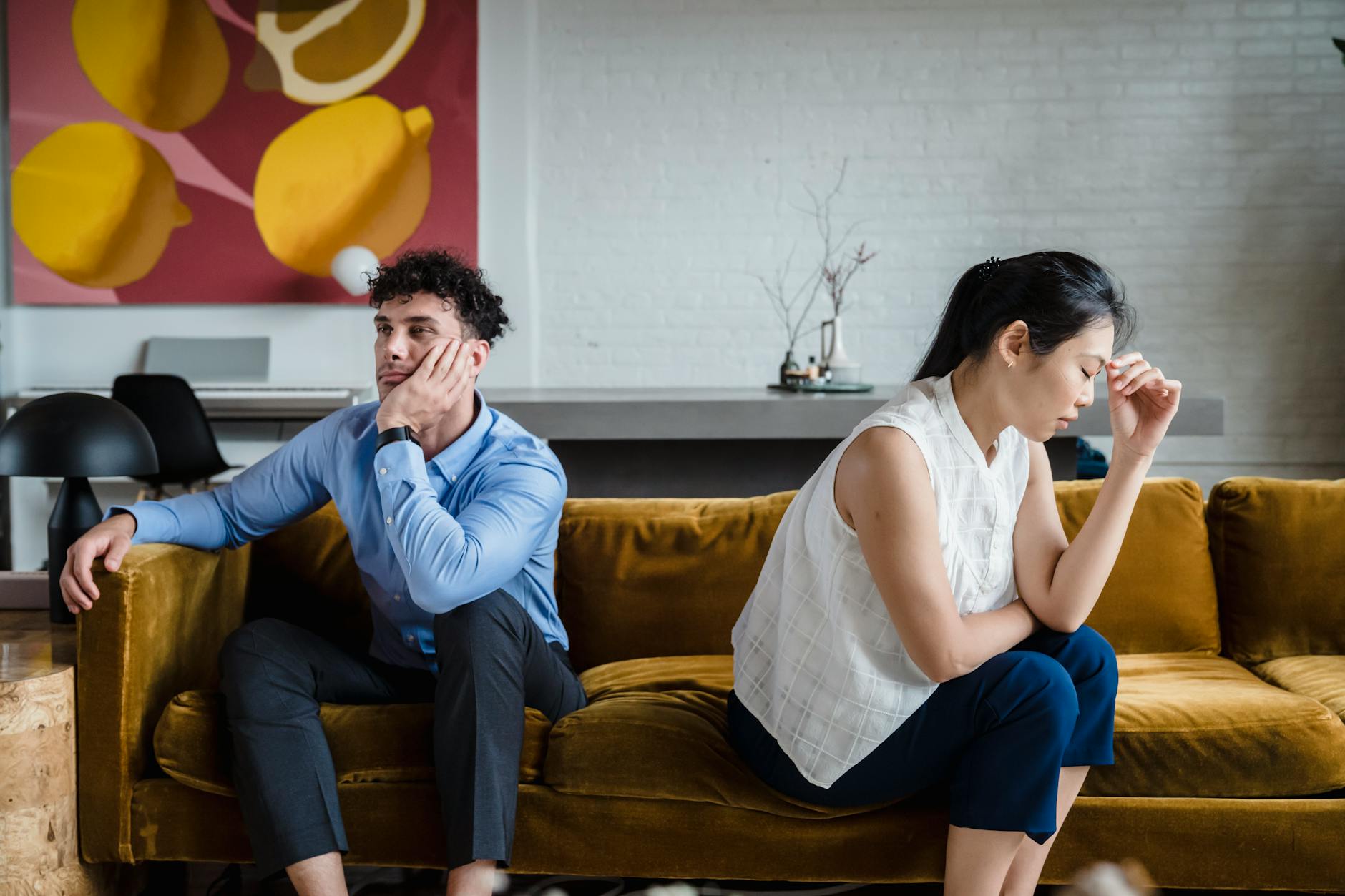 A couple sits apart on a sofa, looking unhappy and deep in thought, reflecting relationship conflict. - declutter relationship conflict