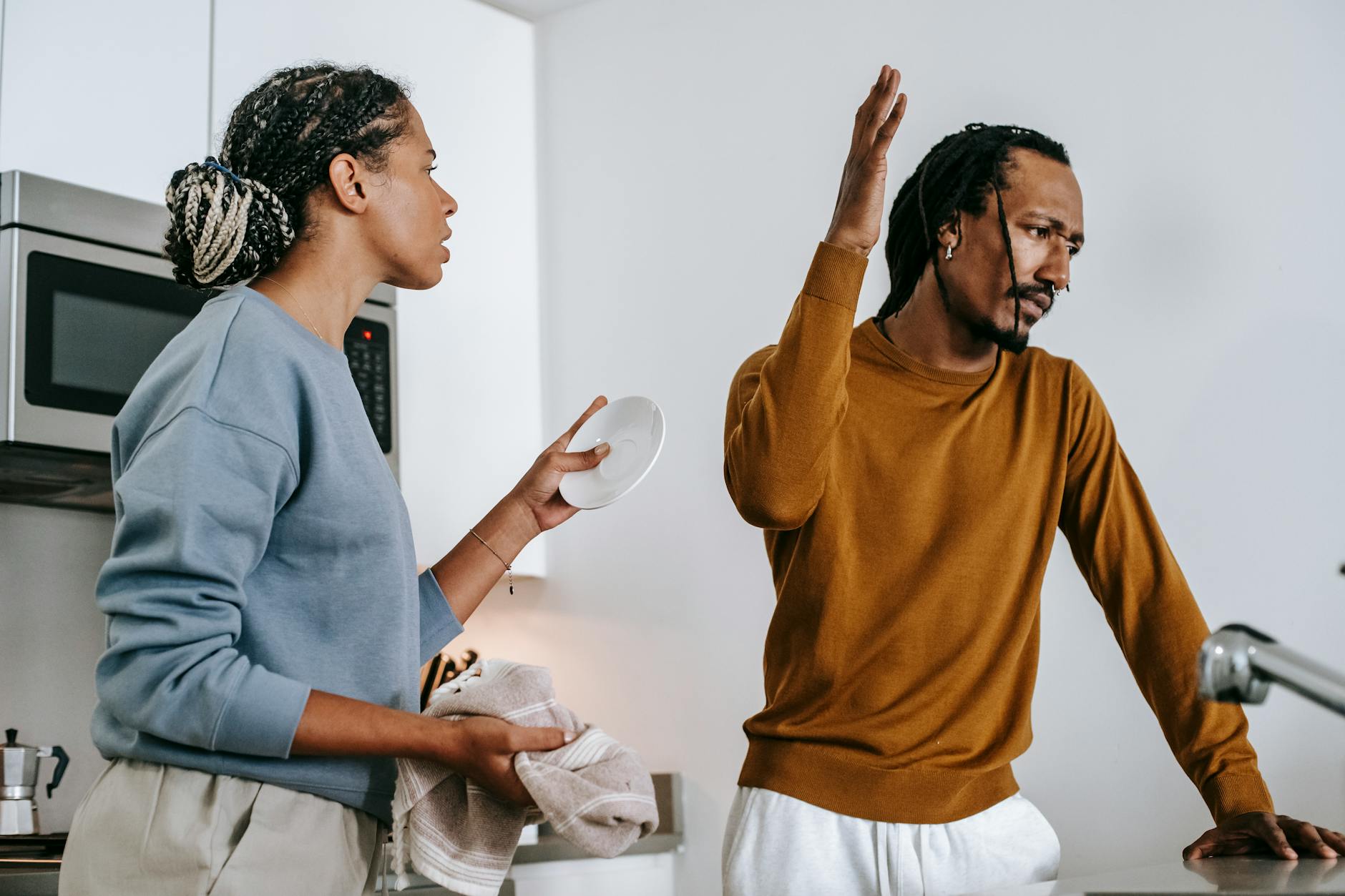 Young dissatisfied African American man with raised arm having conflict with girlfriend in house - declutter relationship conflict
