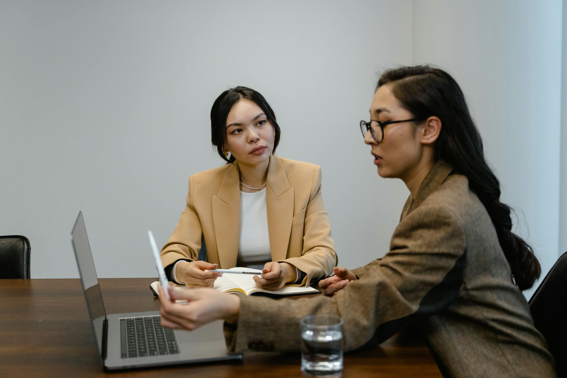 Two Asian businesswomen in a professional meeting discussing work at a conference table. - effective communication skills