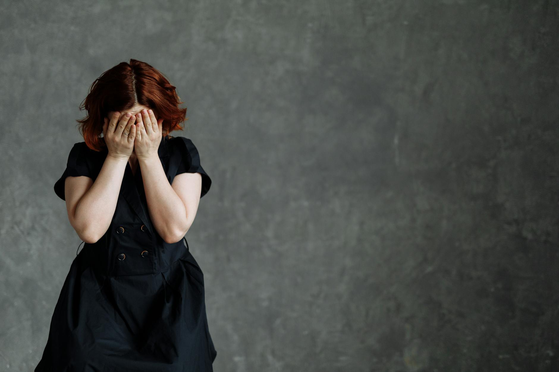 A woman in a black dress expressing emotion against a concrete backdrop, highlighting themes of sadness and stress. - express complex emotions