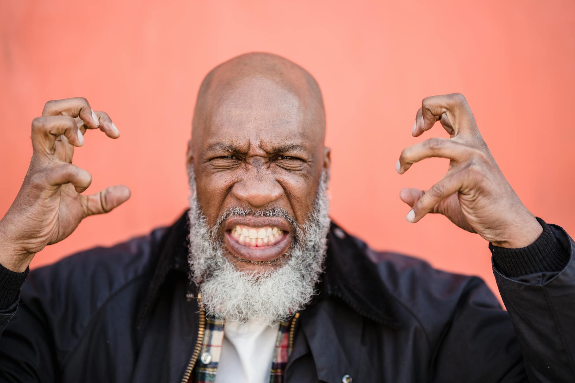 Dynamic portrait capturing strong emotions of an elderly man with a beard against a peach background. - express complex emotions