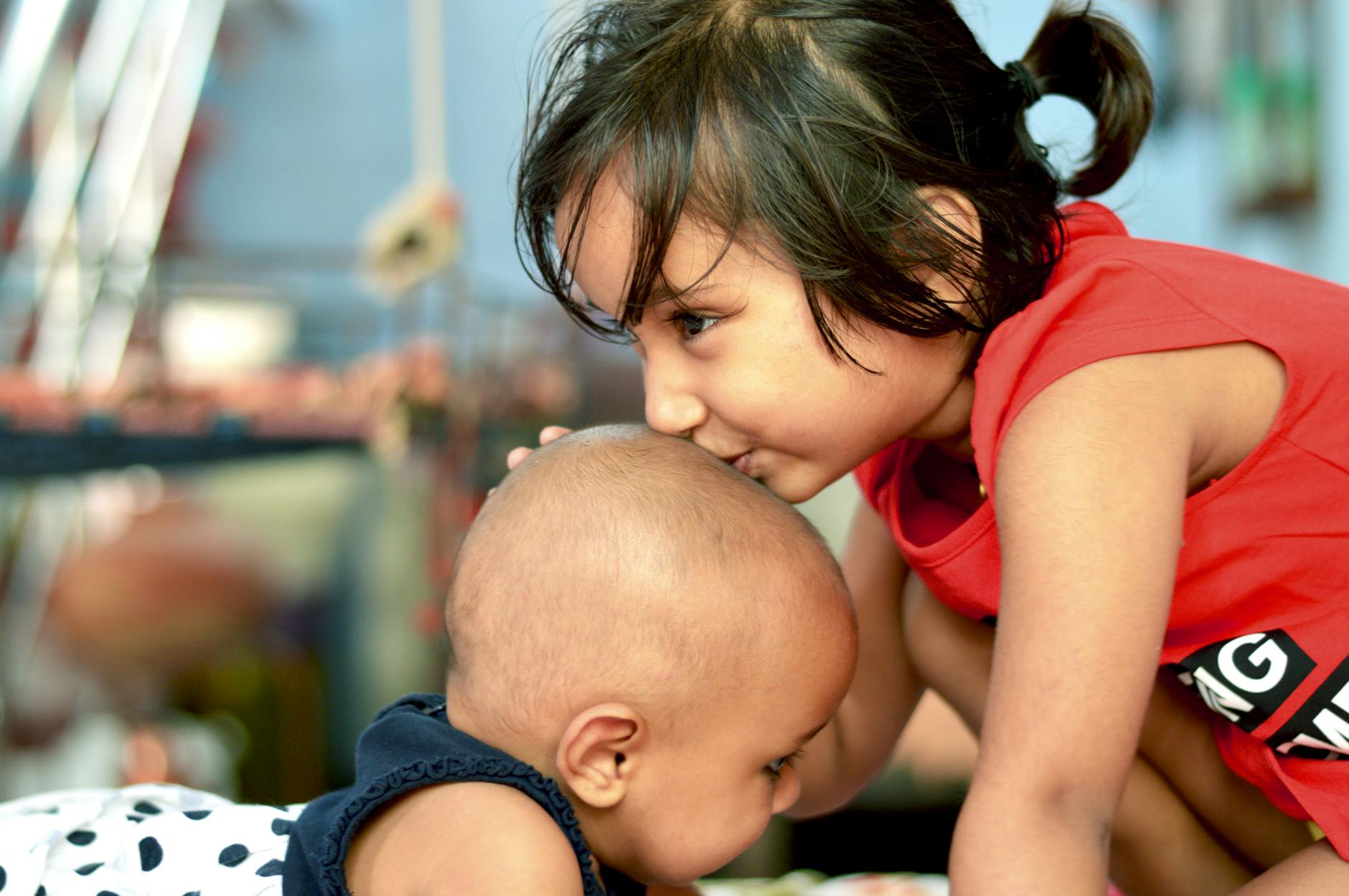 A touching moment of sisterhood as a young girl gently kisses her baby brother's head indoors. - family guy sibling rivalry