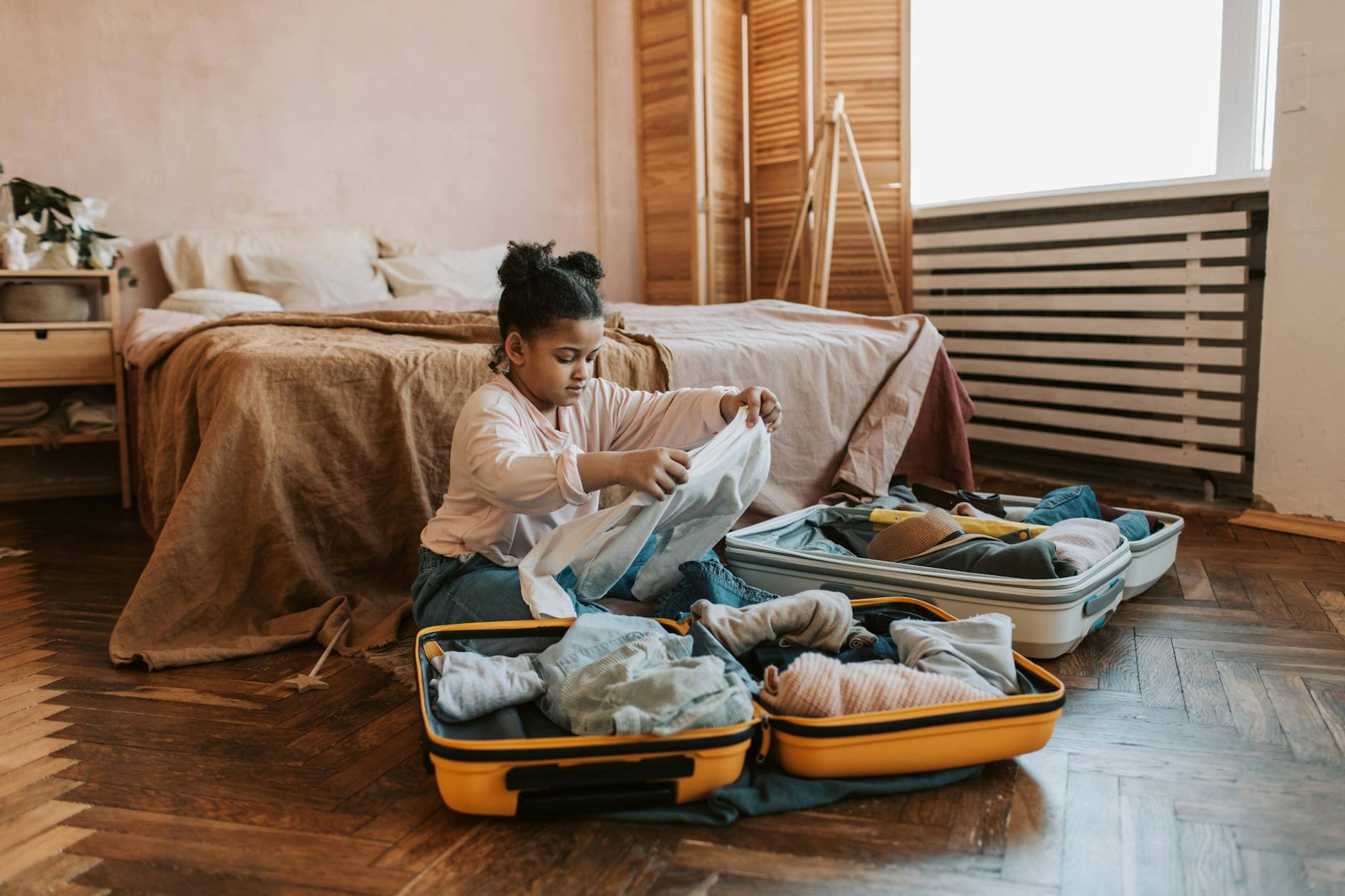 Young girl folding clothes and packing a suitcase in a warm, cozy bedroom. - family travel tips