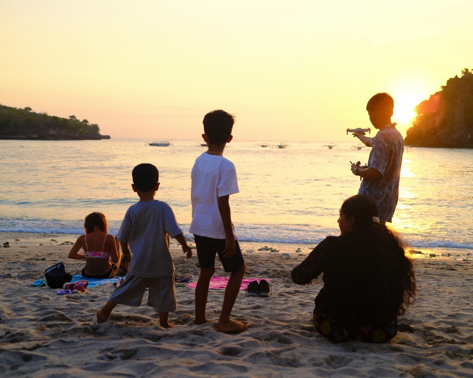 A family enjoys a beautiful sunset on a Bali beach with children playing and adults relaxing. - family travel tips