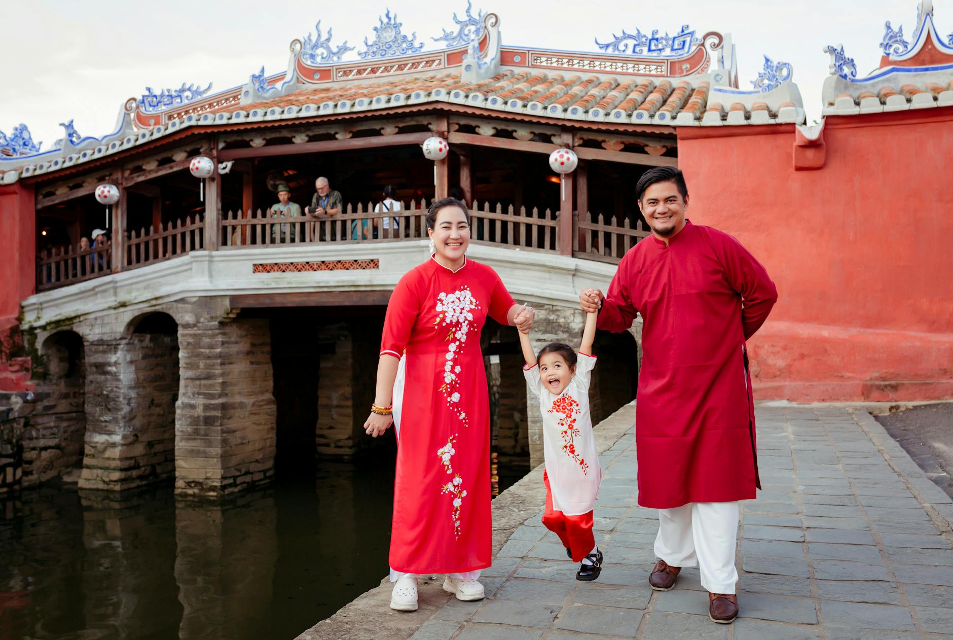 A family wearing red ao dai in front of the Japanese Covered Bridge in Hội An, Vietnam. - family travel tips