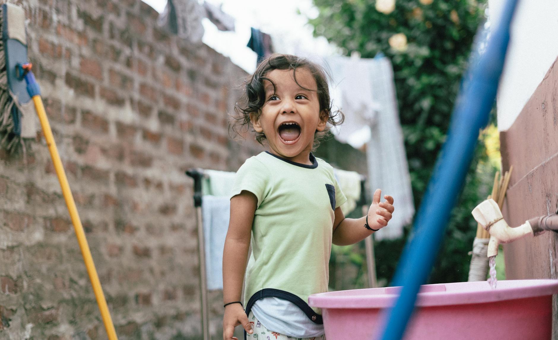 Adorable child with curly hair laughing joyfully near an outdoor faucet. Vibrant and carefree moment. - fostering independence children