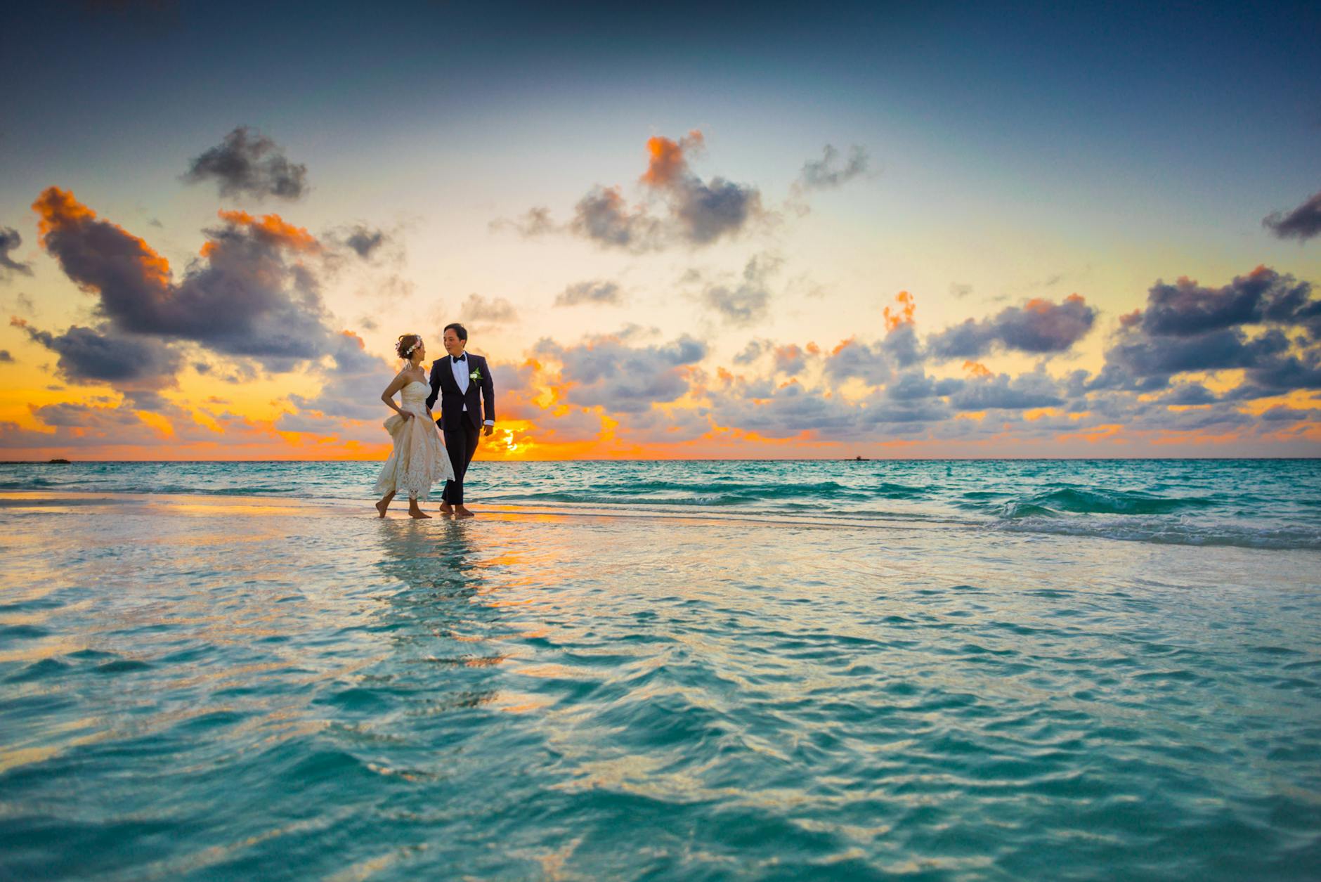 A young couple enjoying a romantic beach wedding during a vibrant sunset. - future goals couple