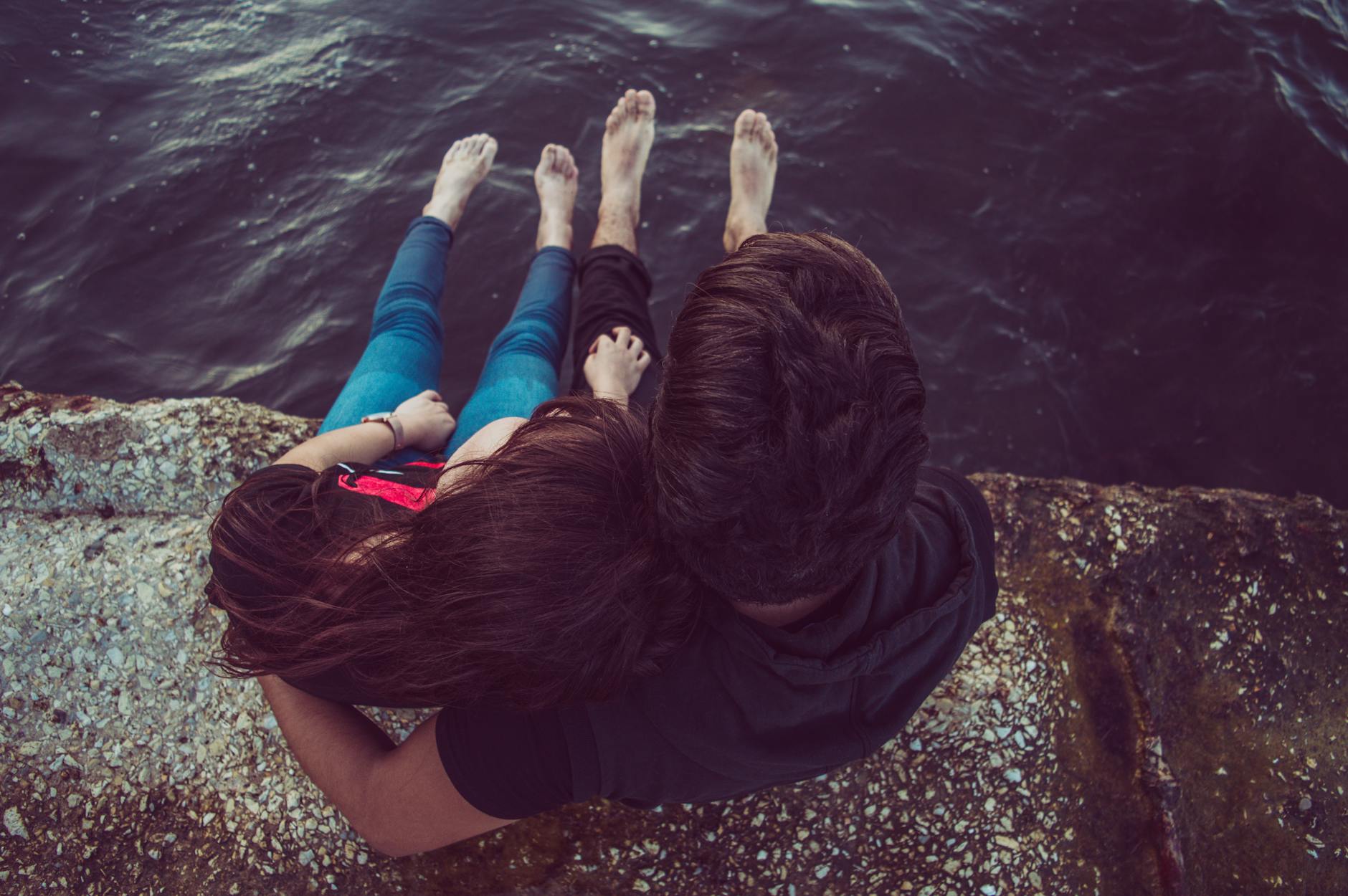 A romantic couple sitting on a rocky pier, enjoying a serene moment by the water. - future goals couple