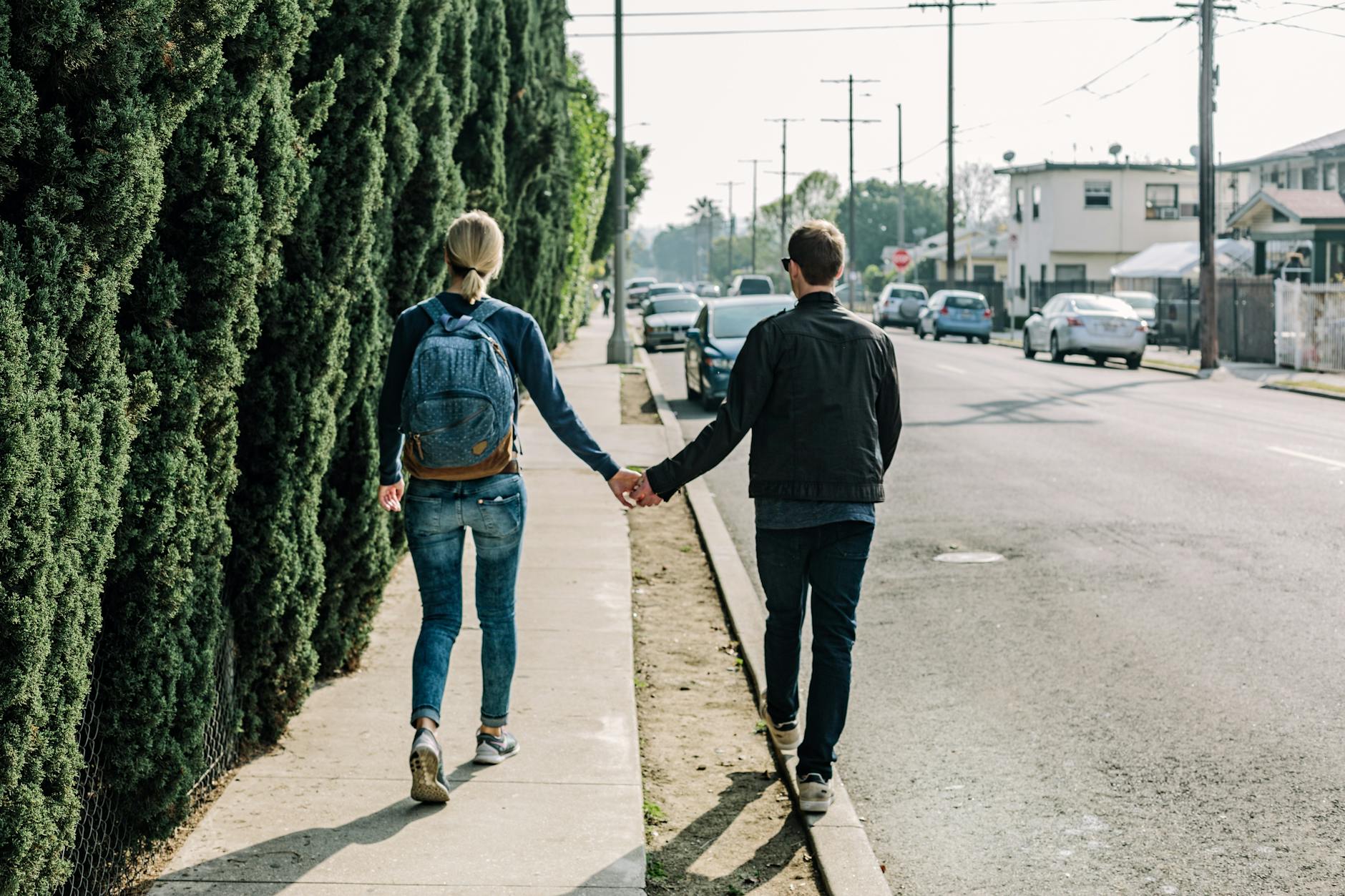 A couple walks hand in hand along a sunny sidewalk in an urban area, showcasing romance and companionship. - future goals couple