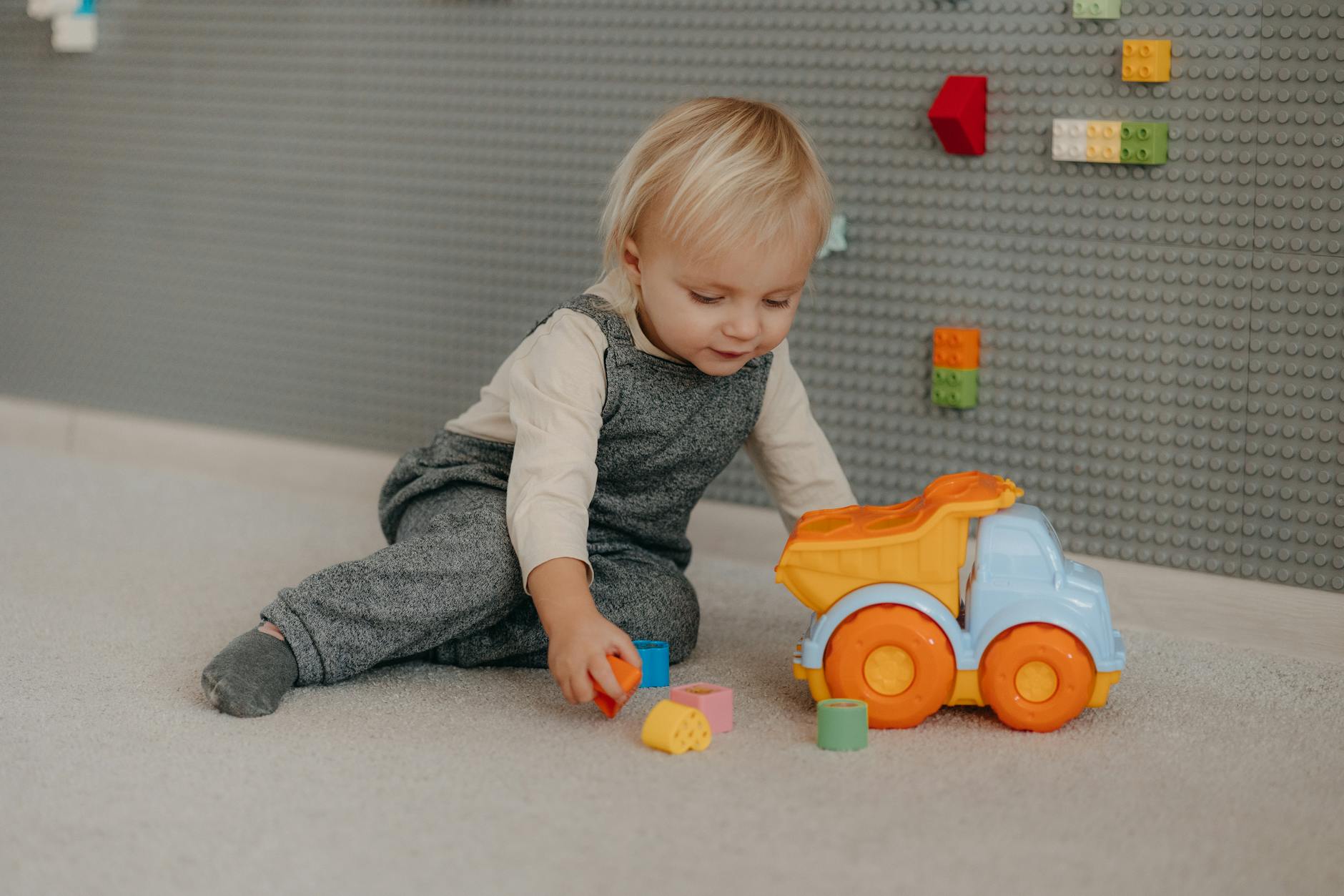 Cute toddler engaged with colorful blocks and toy truck indoors. - independent play toddler