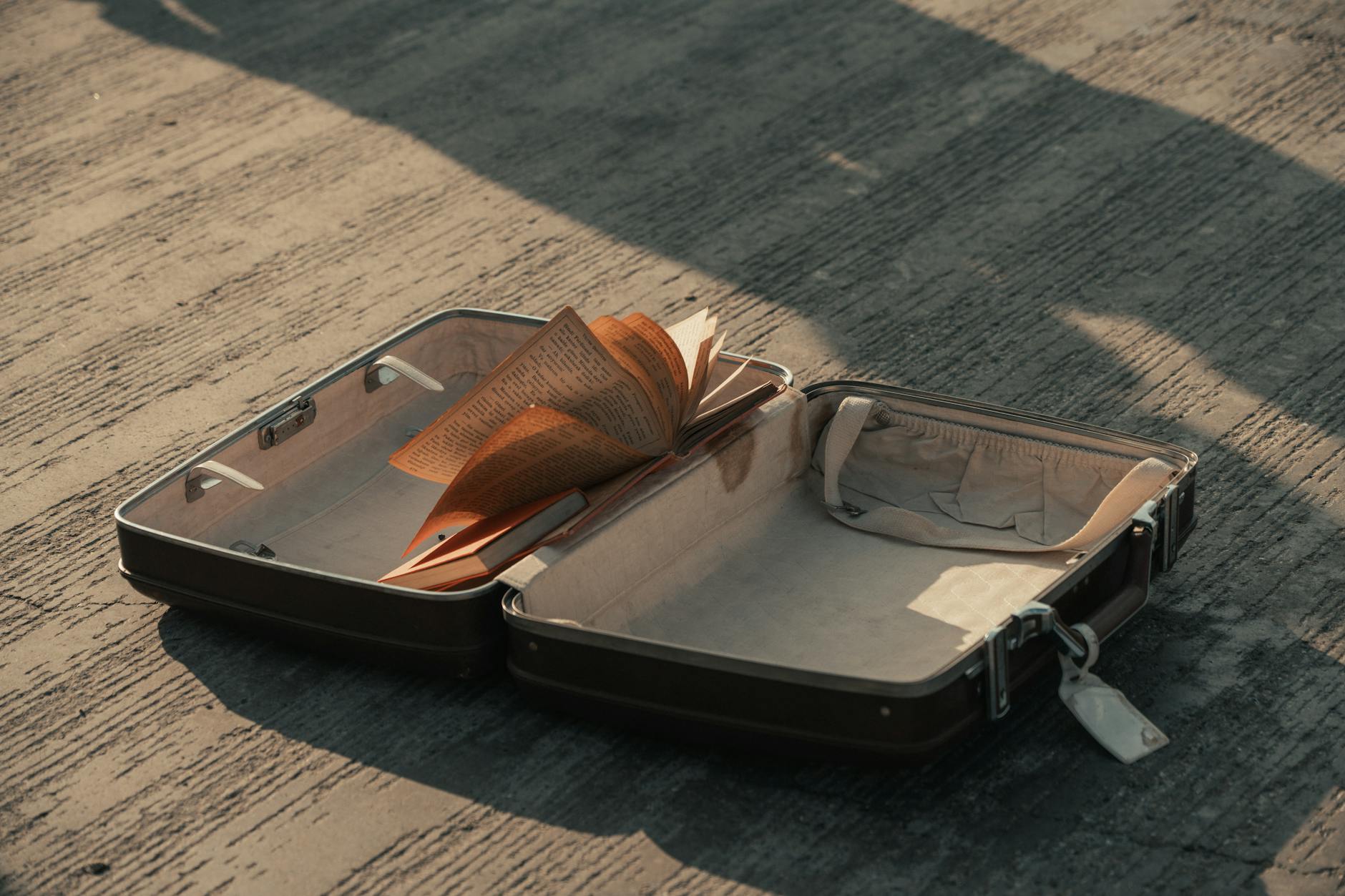 An open suitcase with a book lying on a concrete surface, casting a shadow. - letting go of baggage