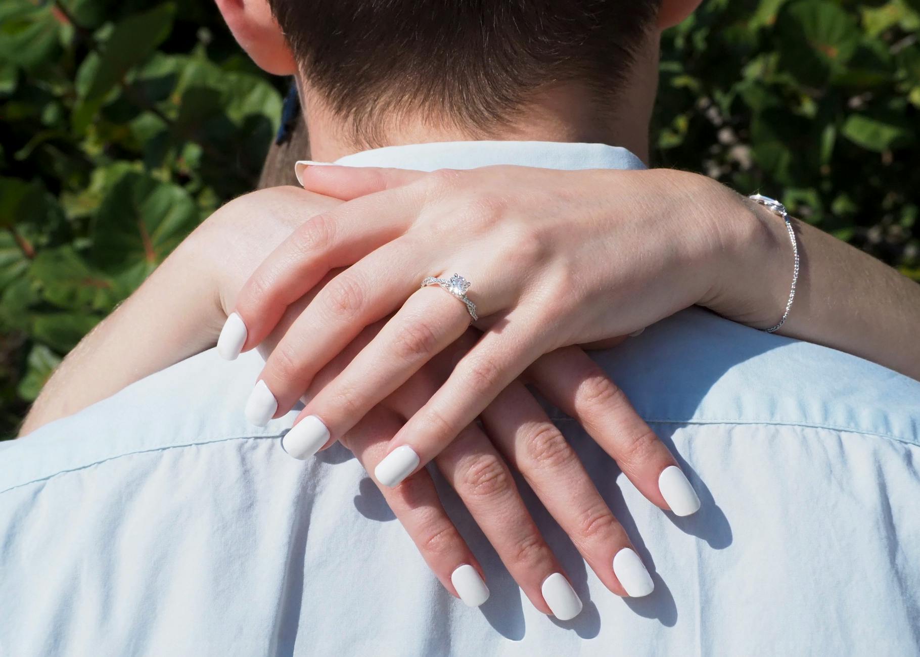 Close-up of a couple embracing, showcasing a diamond engagement ring during a sunny day. - marriage goals spring