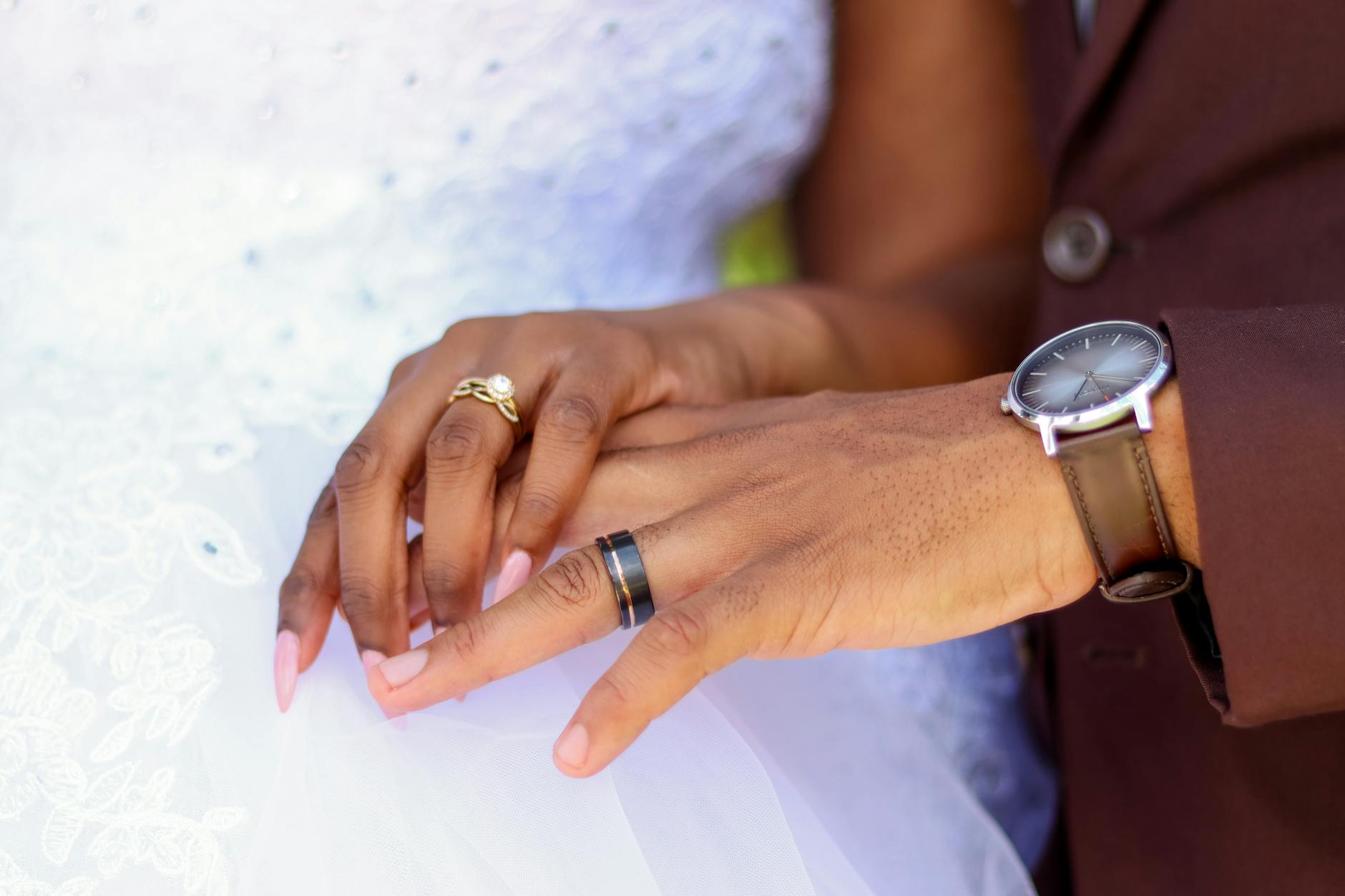 Close-up of newlywed couple holding hands, showcasing wedding rings and elegant outfits. - marriage joy rediscovery
