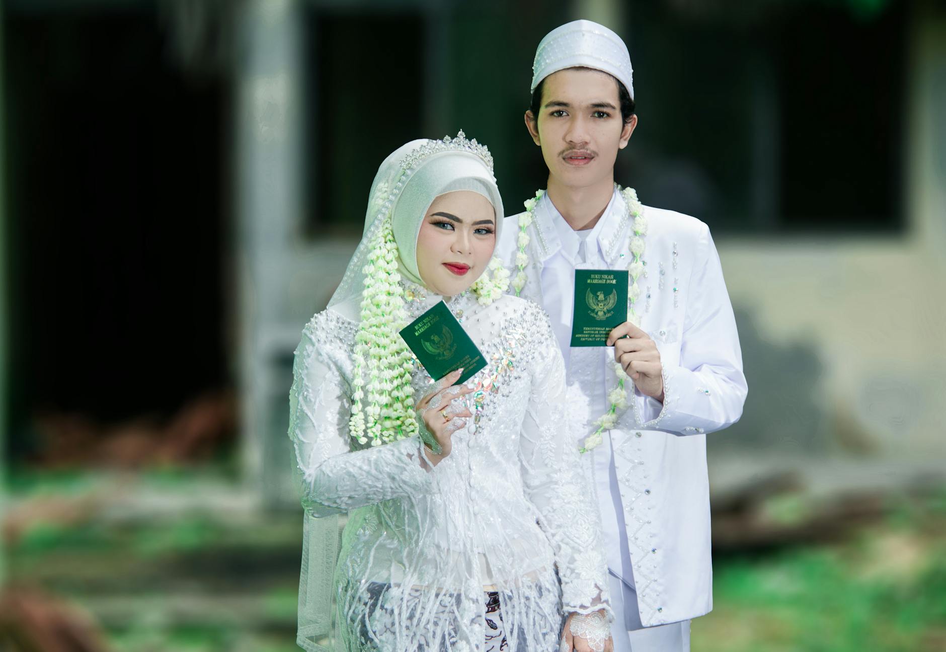 A joyful Indonesian couple celebrating their Muslim wedding in traditional attire, holding marriage certificates. - marriage traditions