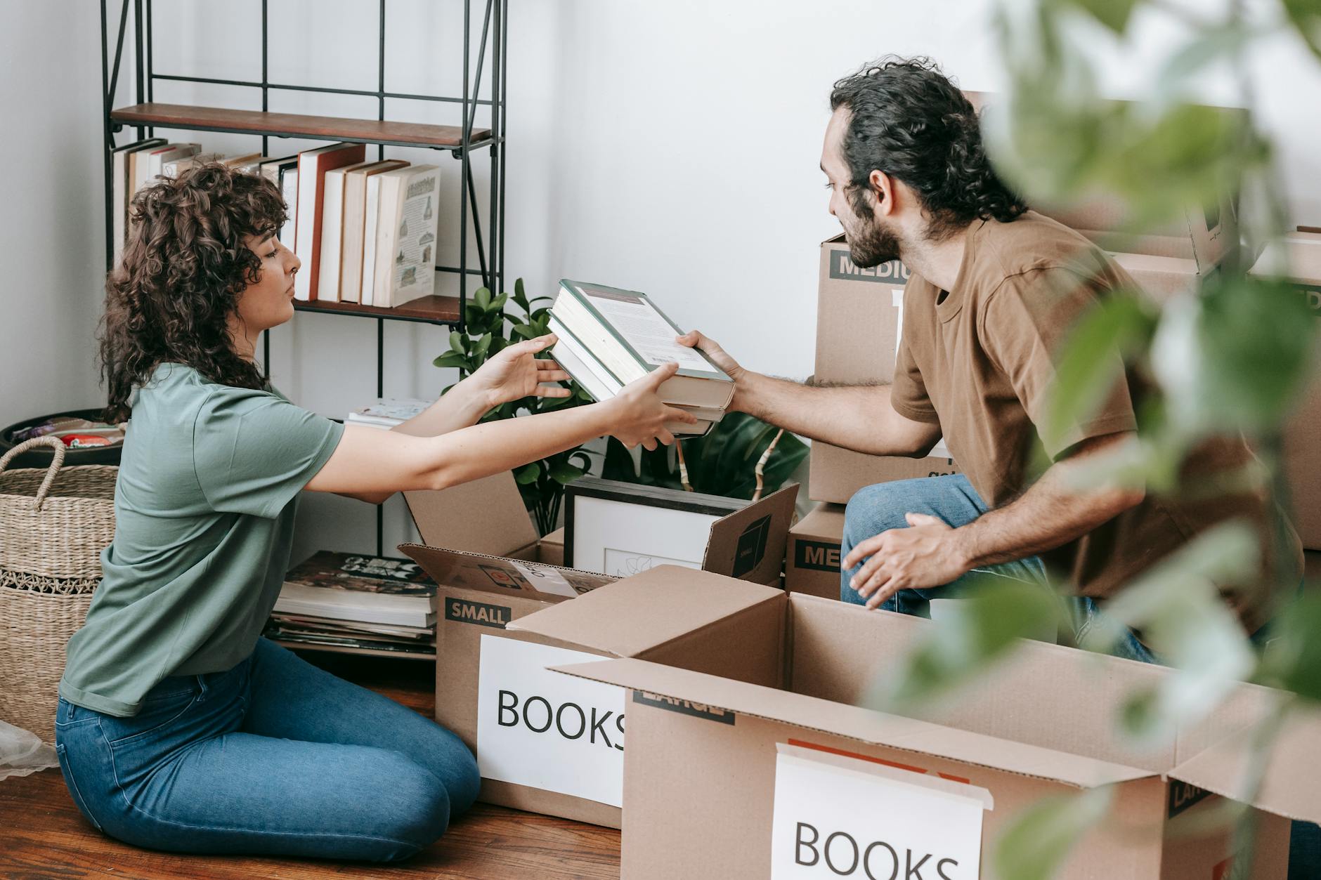 A couple organizing and packing books in cardboard boxes indoors, preparing for a move. - mental health decluttering