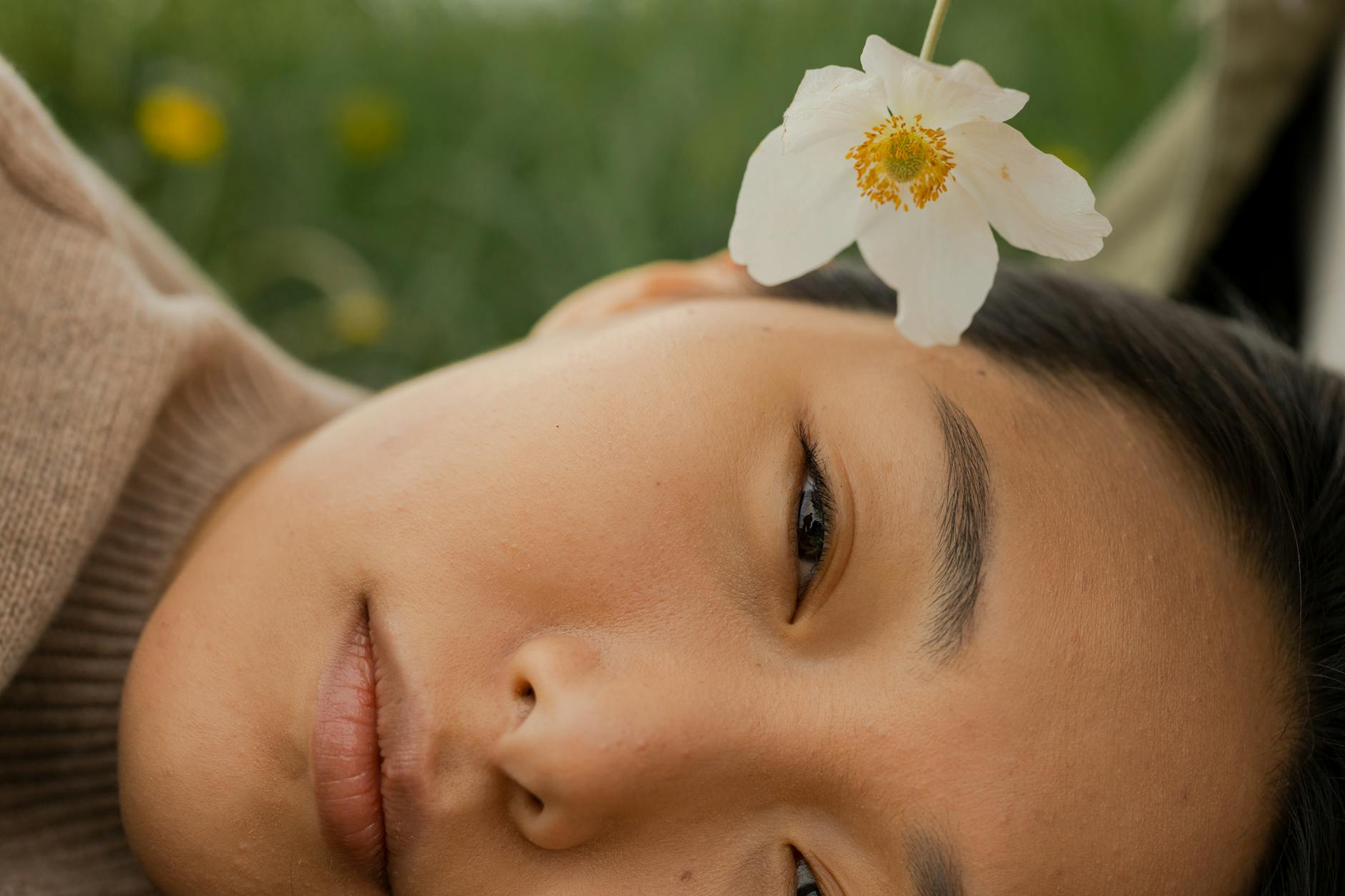 Close-up of a serene woman lying outdoors with a white flower. - mindfulness spring allergies