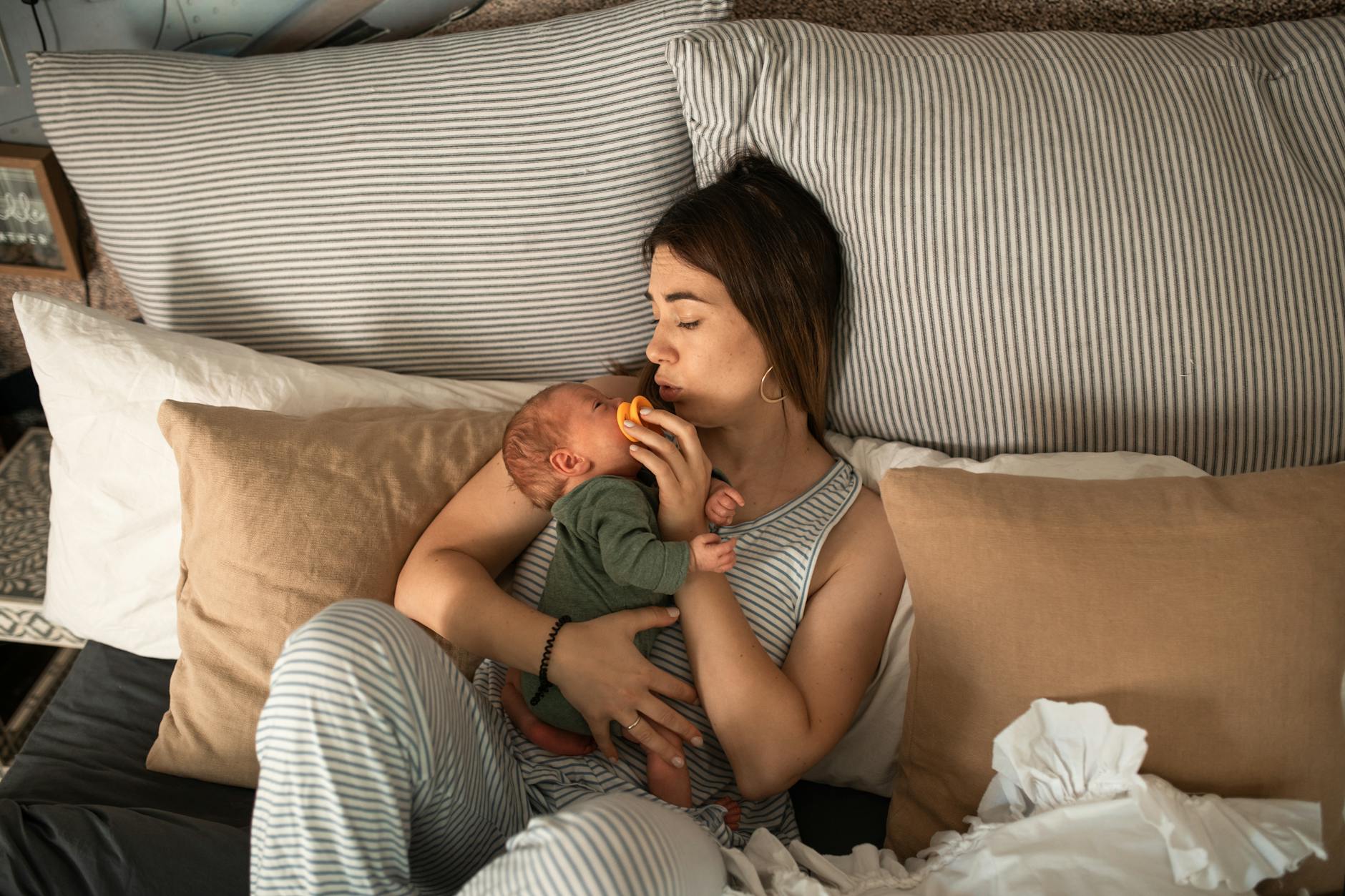 Mother tenderly holding her newborn while relaxing in a cozy bedroom setting, capturing a moment of warmth and care. - new parent exhaustion