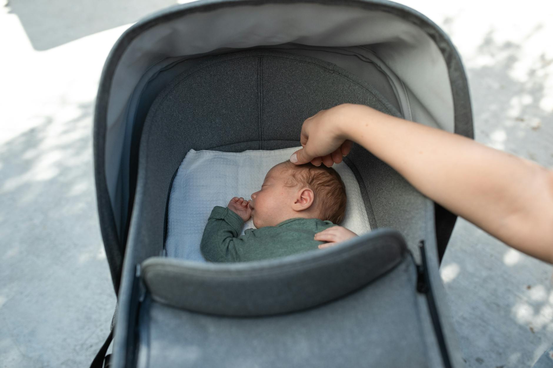 A serene moment of a baby sleeping in a stroller with a gentle touch from an adult hand. - new parent exhaustion