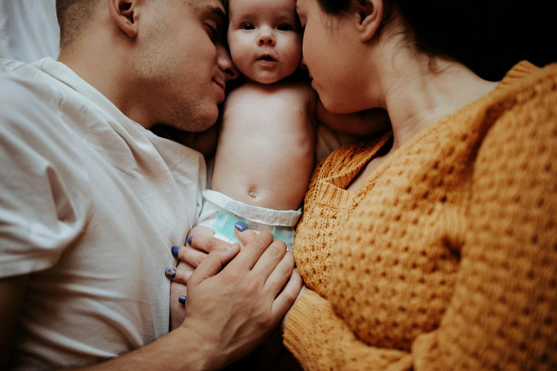 A tender family moment with parents embracing their infant in bed, showcasing love and intimacy. - new parent self care