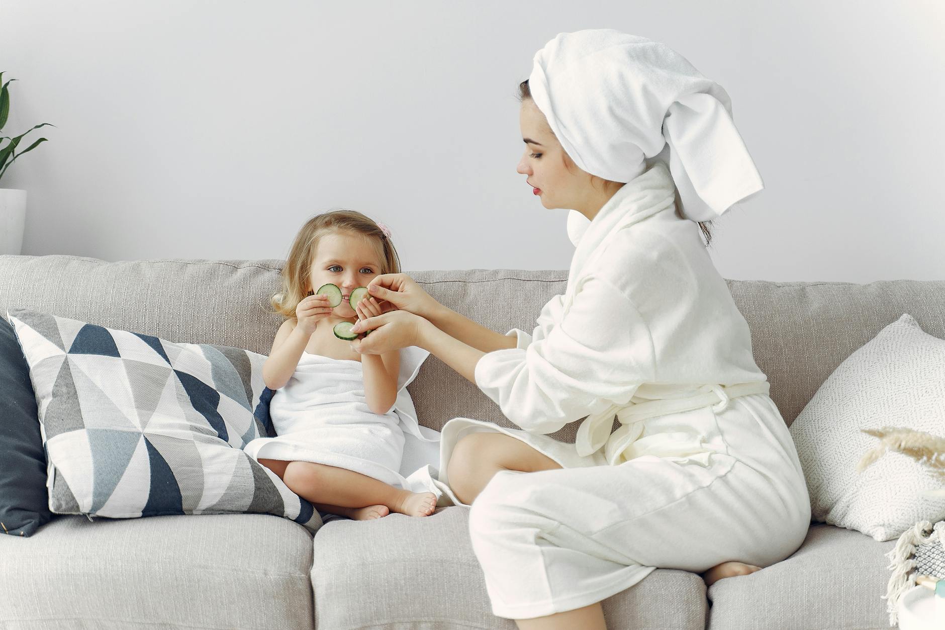A mother and daughter enjoy a spa day at home, bonding on the couch with cucumber slices. - new parent self care