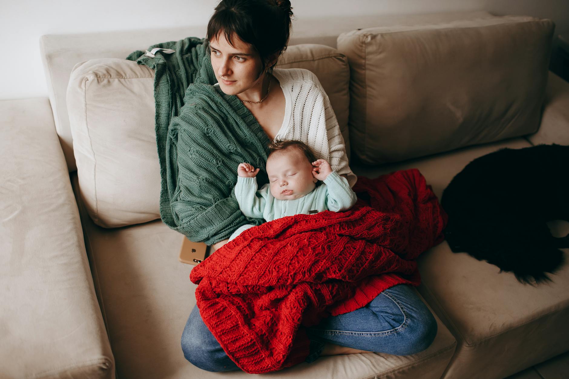 A mother lovingly holding her baby on a cozy sofa, wrapped in warm blankets. - new parent self care