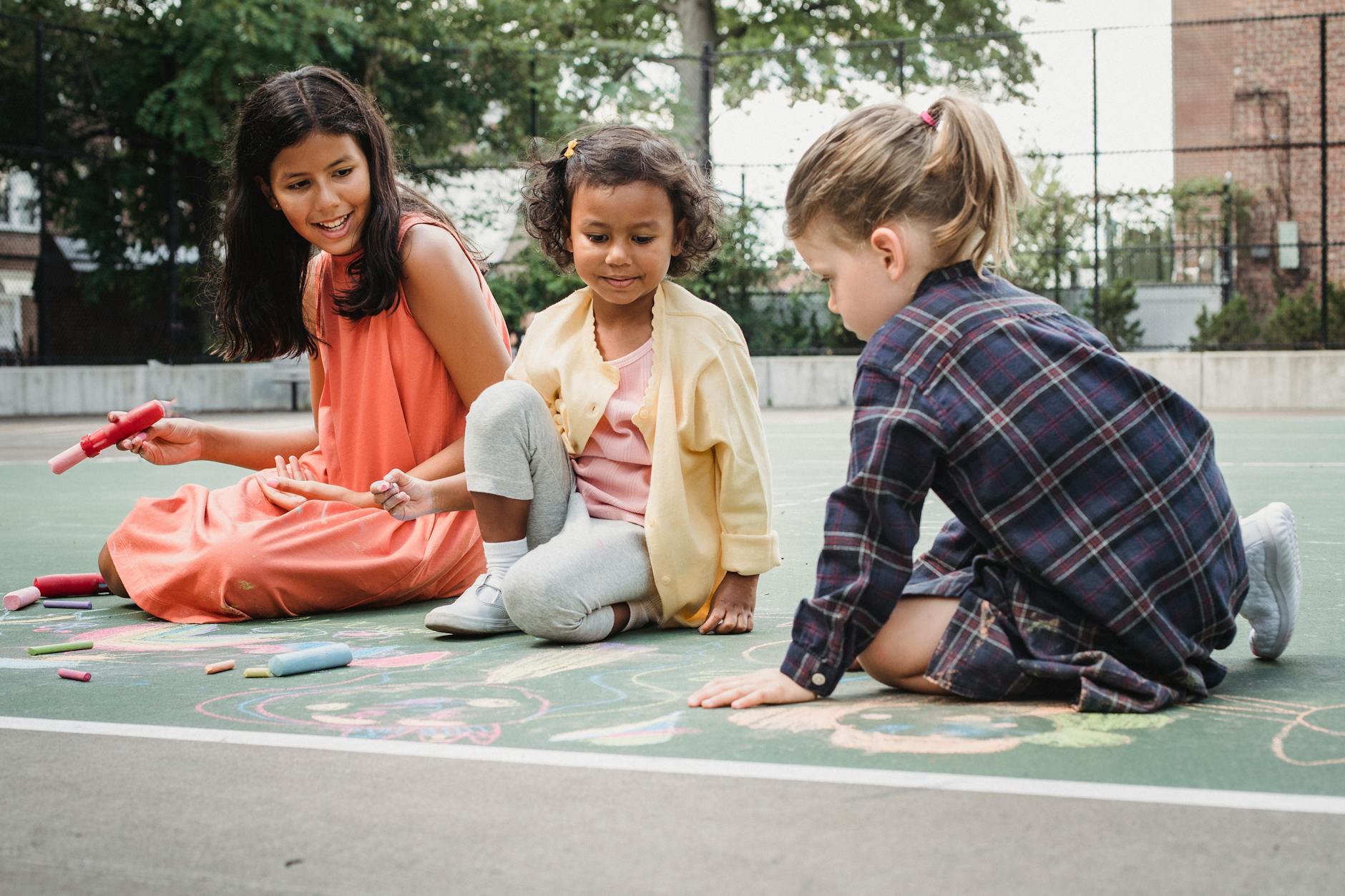 Three children drawing with chalk on a sunny outdoor court. Fun and creativity in action. - outdoor social skills