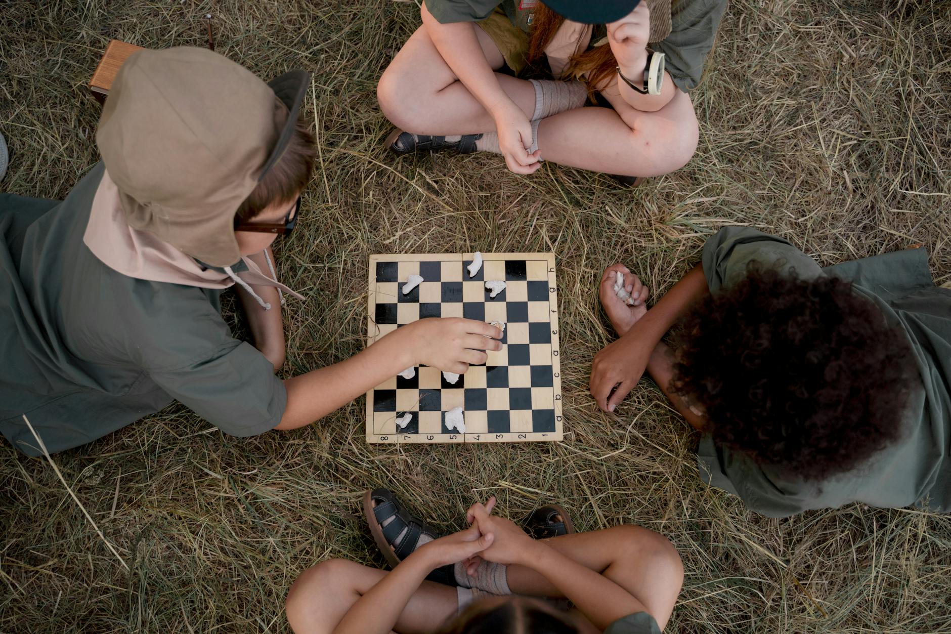 A group of kids playing chess on grass, enjoying a strategic game in summertime. - outdoor social skills