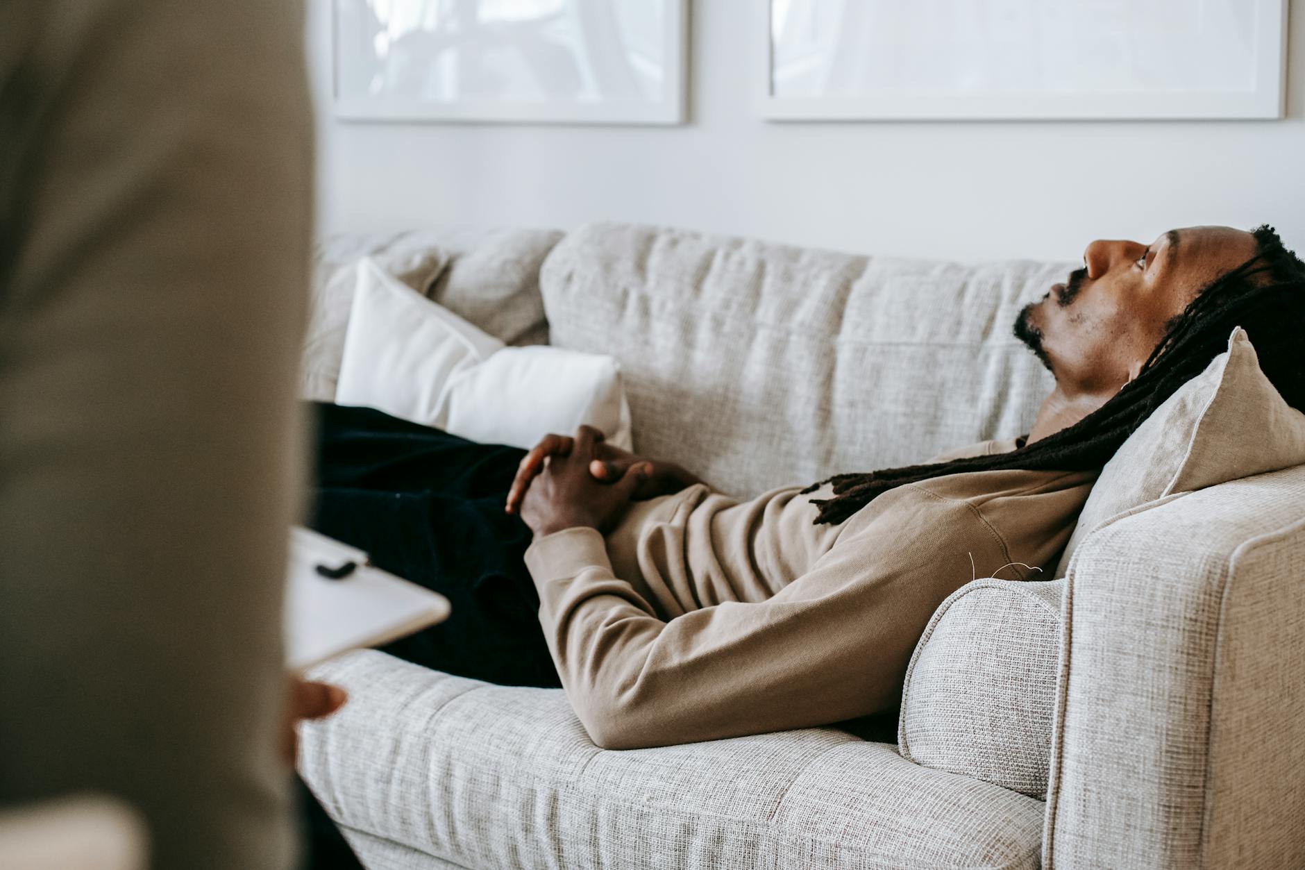 Crop contemplative African American male with dreadlocks relaxing on soft couch and listening to skilled counselor advices during psychotherapy - overthinking therapy