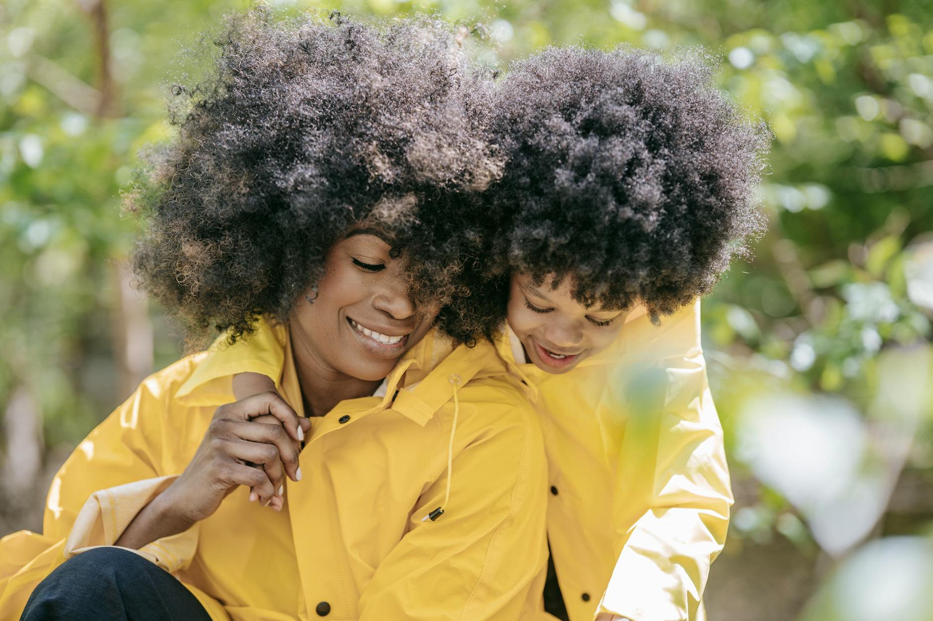 Smiling mother and daughter bundled up in matching yellow raincoats enjoying a sunny day outdoors. - parental burnout spring