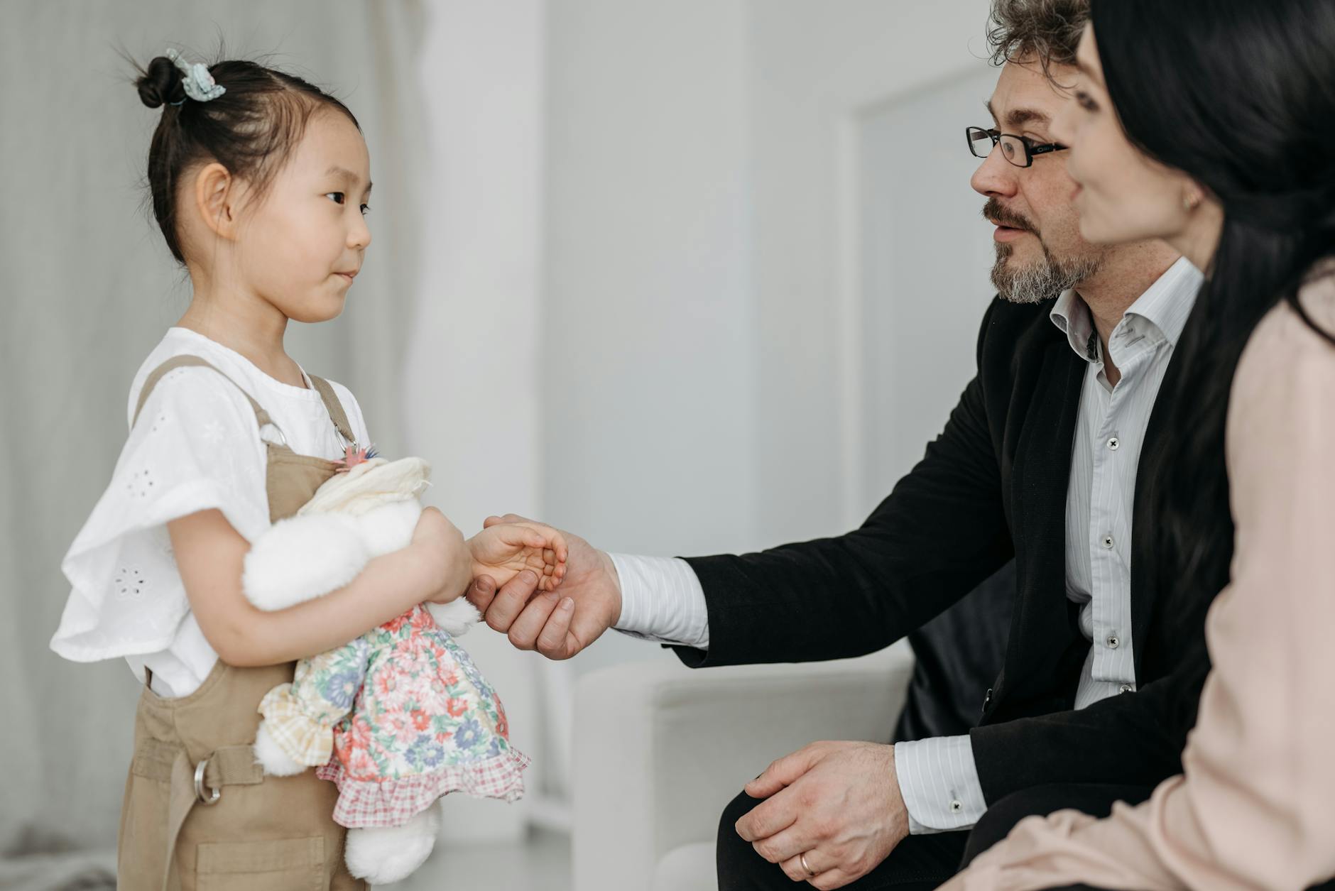 A joyful moment of a couple adopting a young Asian girl holding a teddy bear indoors. - partner communication family