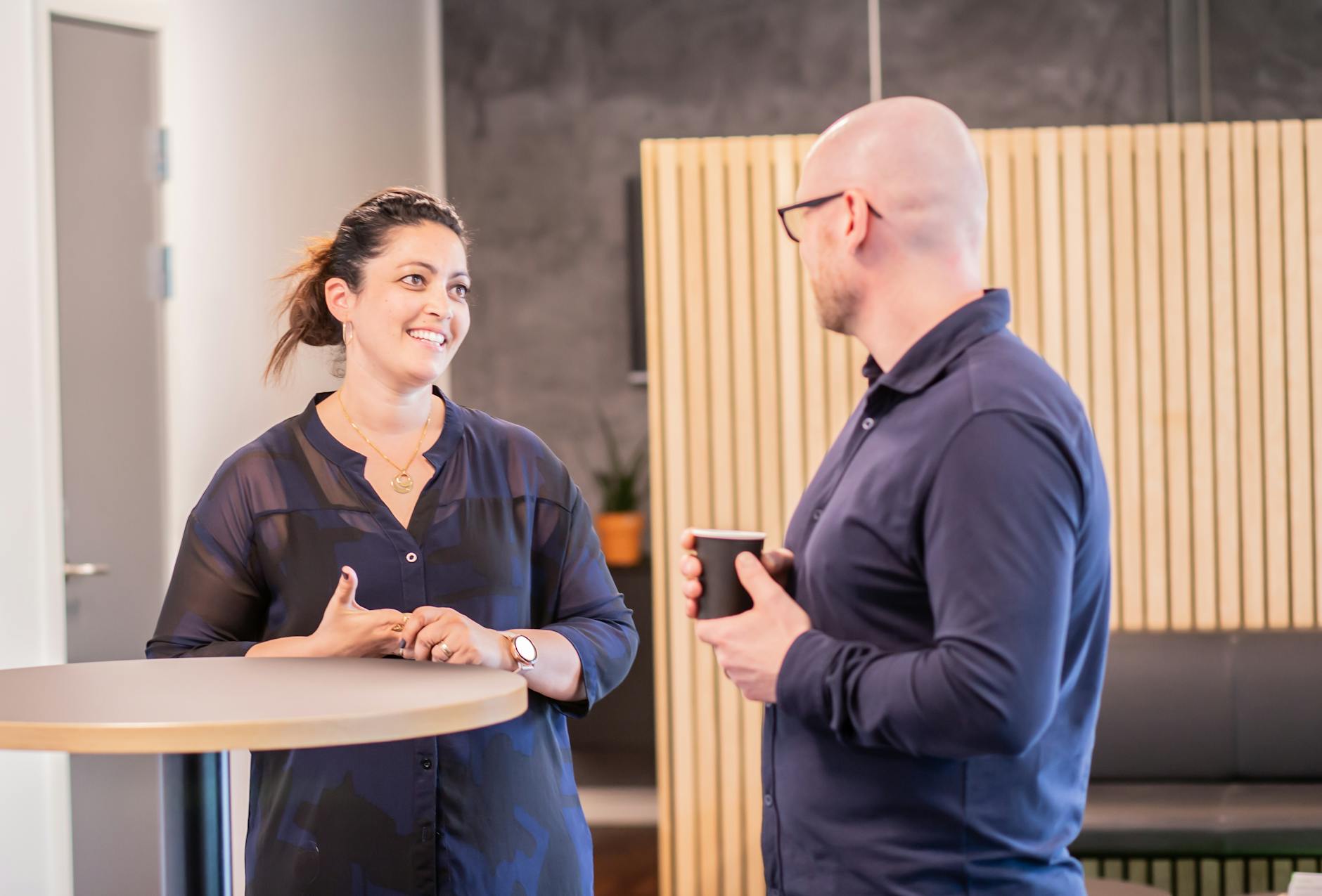 Two coworkers engage in a friendly conversation over coffee in a modern office setting. - post-break communication