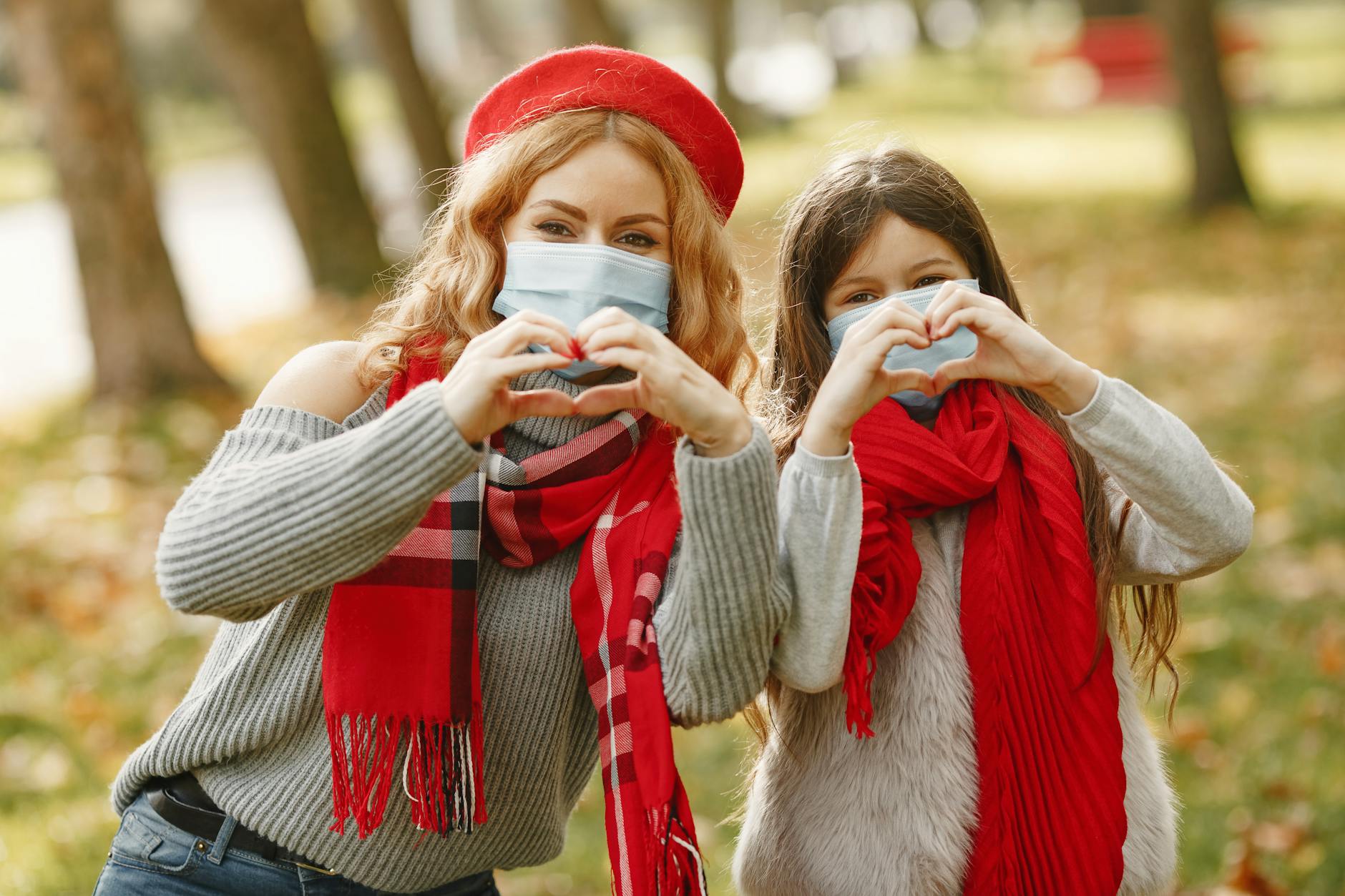 Mother and daughter making heart symbols in a park wearing masks, expressing love and safety. - post pandemic family