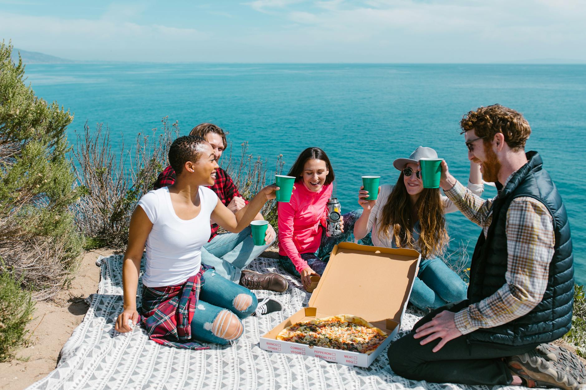 Group of friends enjoying a picnic by the seaside with pizza and drinks on a sunny day. - post spring break reconnect