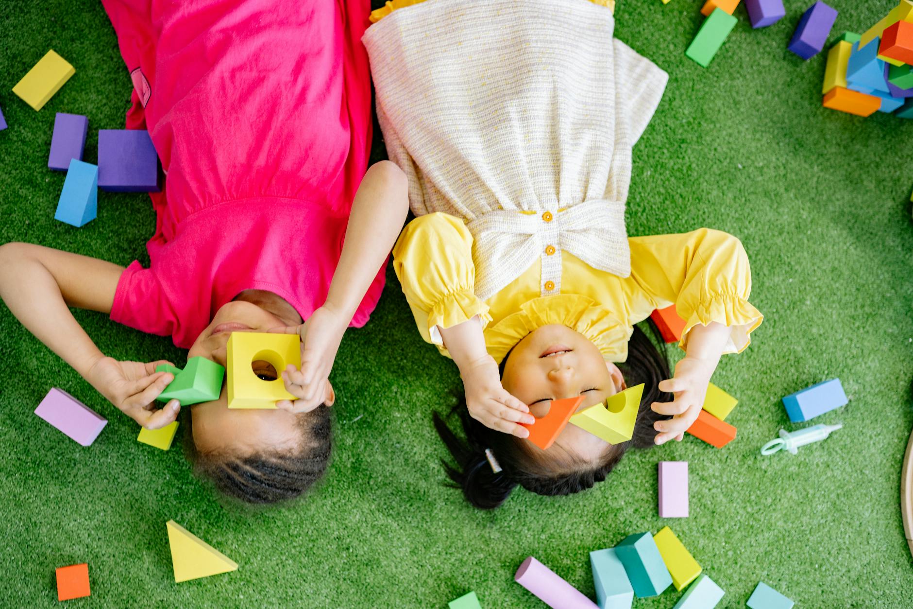 Two joyful kids playing with colorful wooden blocks on a green surface indoors. - preschool spring activities