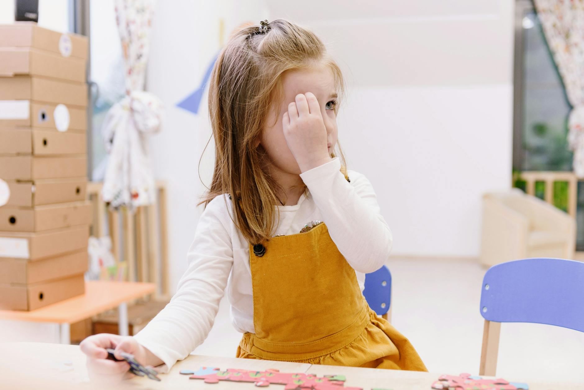 A young girl in a mustard dress plays with a puzzle at a preschool wooden table indoors. - preschooler spring adjustment