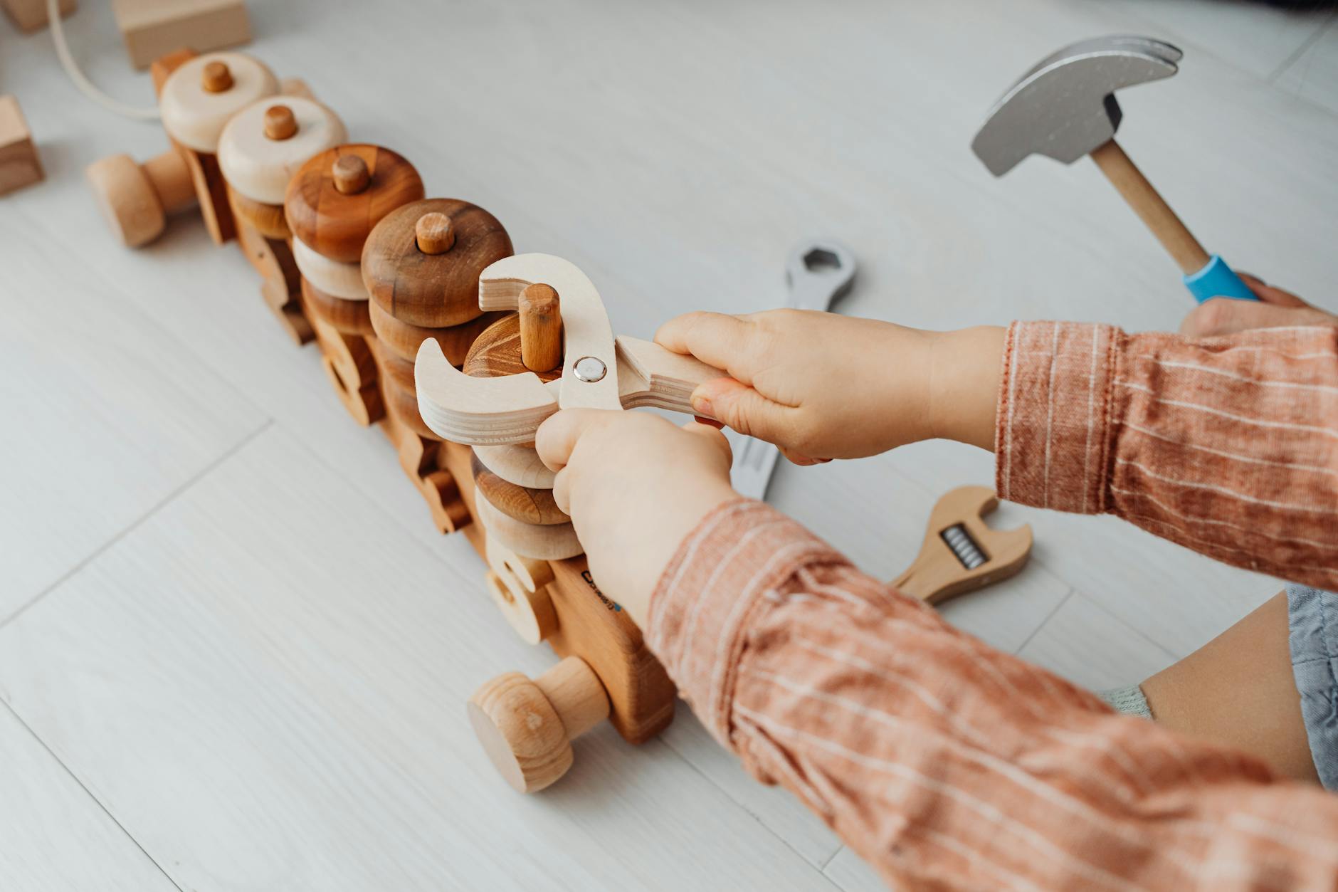 A young child using toy tools to play with a wooden train indoors. Creative playtime. - preschooler spring adjustment