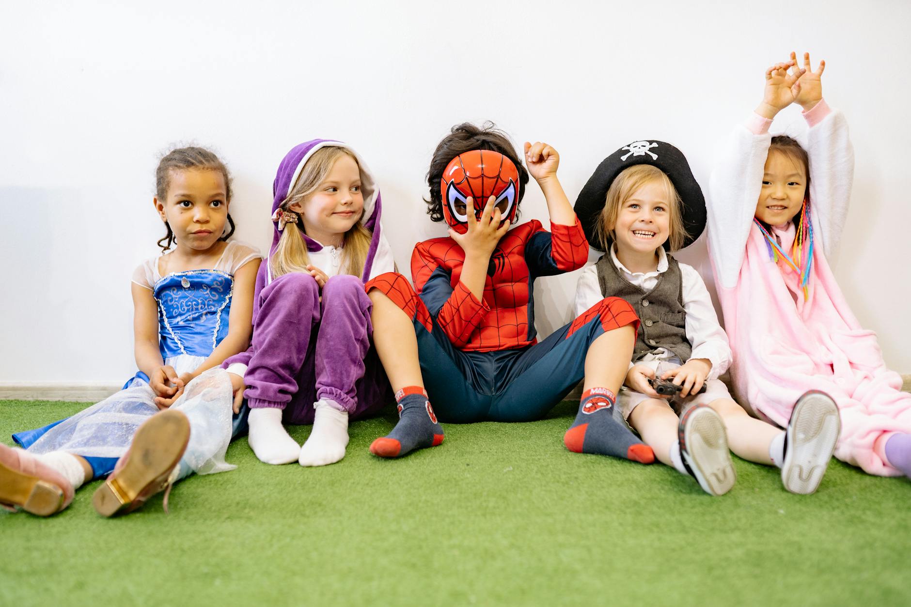 A group of children in various costumes enjoying playtime indoors on a green carpet. - preschooler spring play