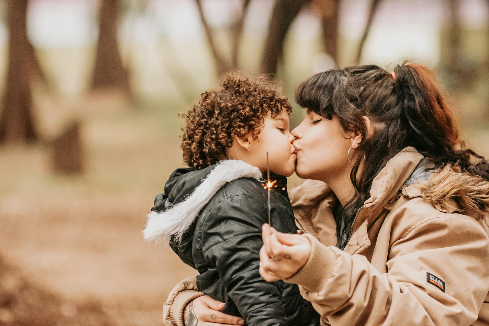 A mother and child share a tender kiss outdoors, holding a sparkler in a cozy autumn setting. - reignite relationship spark