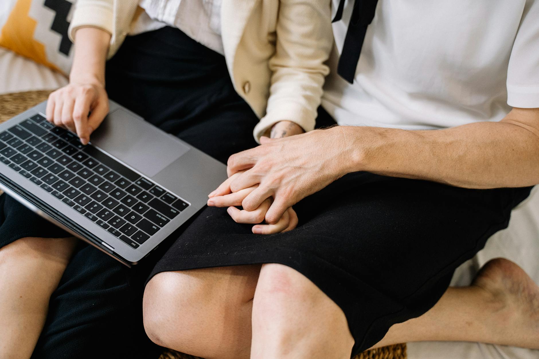 A close-up of a couple sitting together, using a laptop while holding hands. - relationship needs communication
