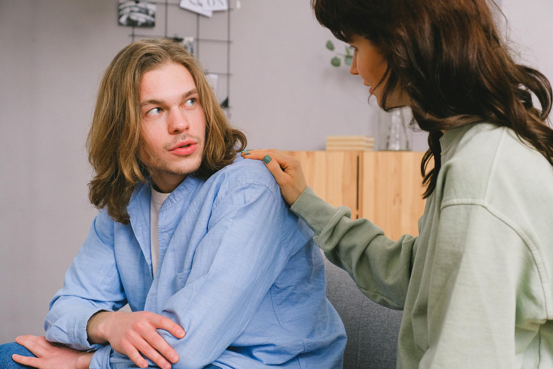 Concentrated woman talking and touching shoulder of pensive male in light room in daytime - relationship needs communication