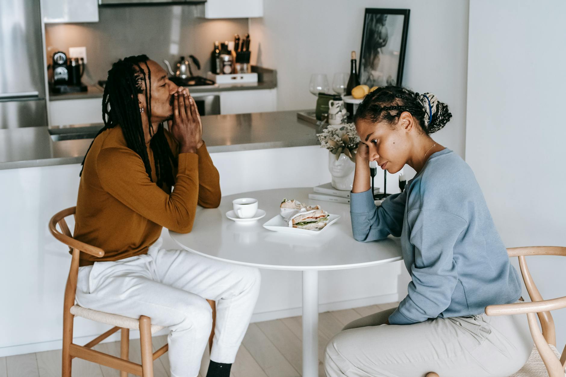 Young African American man sitting at table with woman and looking down thoughtfully while having conflict - relationship needs communication