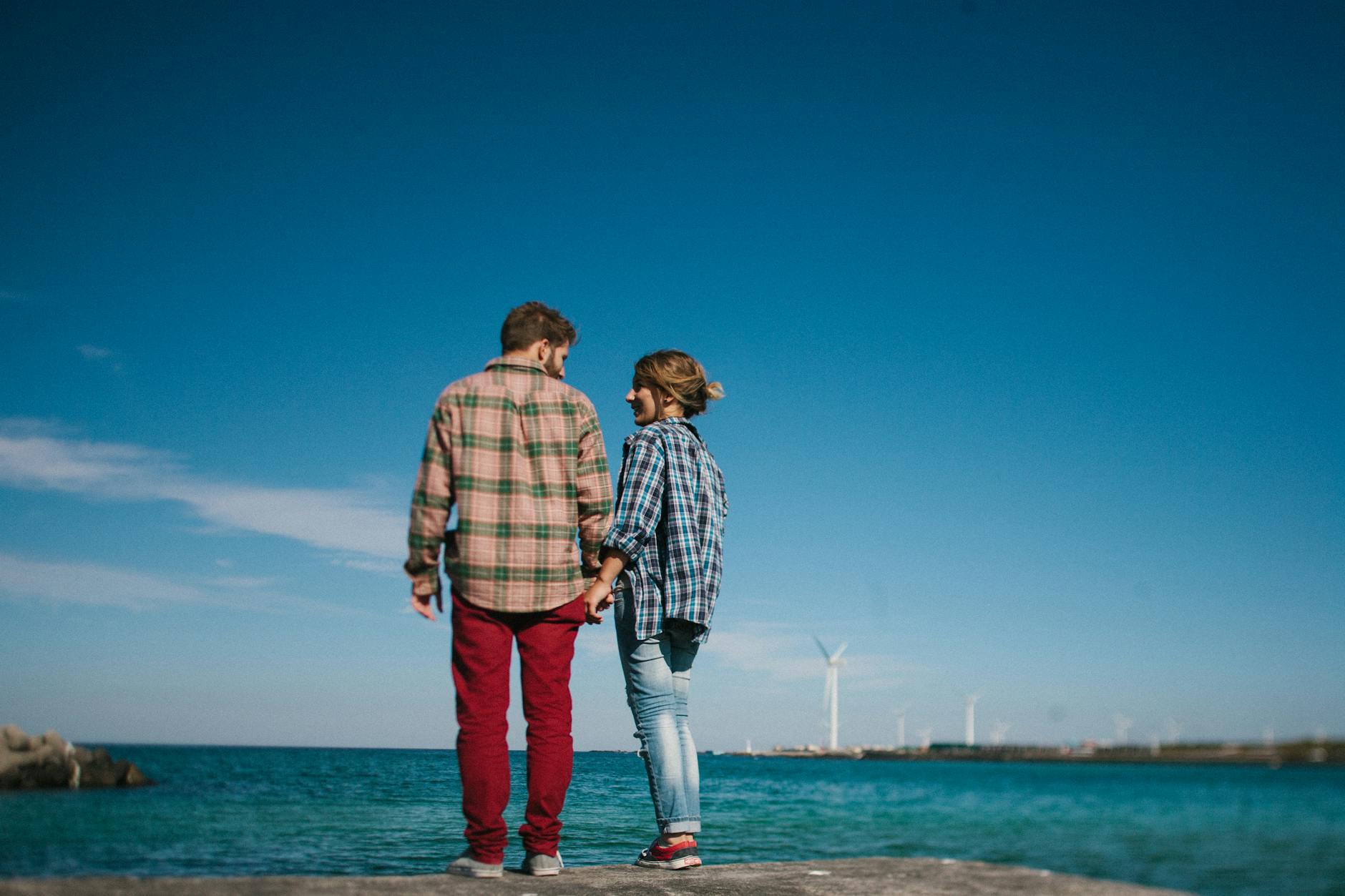 A couple holding hands on a pier with wind turbines and ocean view. - relationship renewal therapy