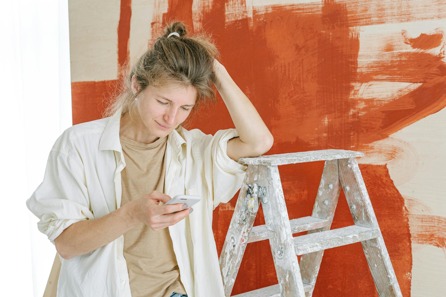 A woman taking a break during home renovation, using her phone near a stepladder and painted wall. - renovation communication needs