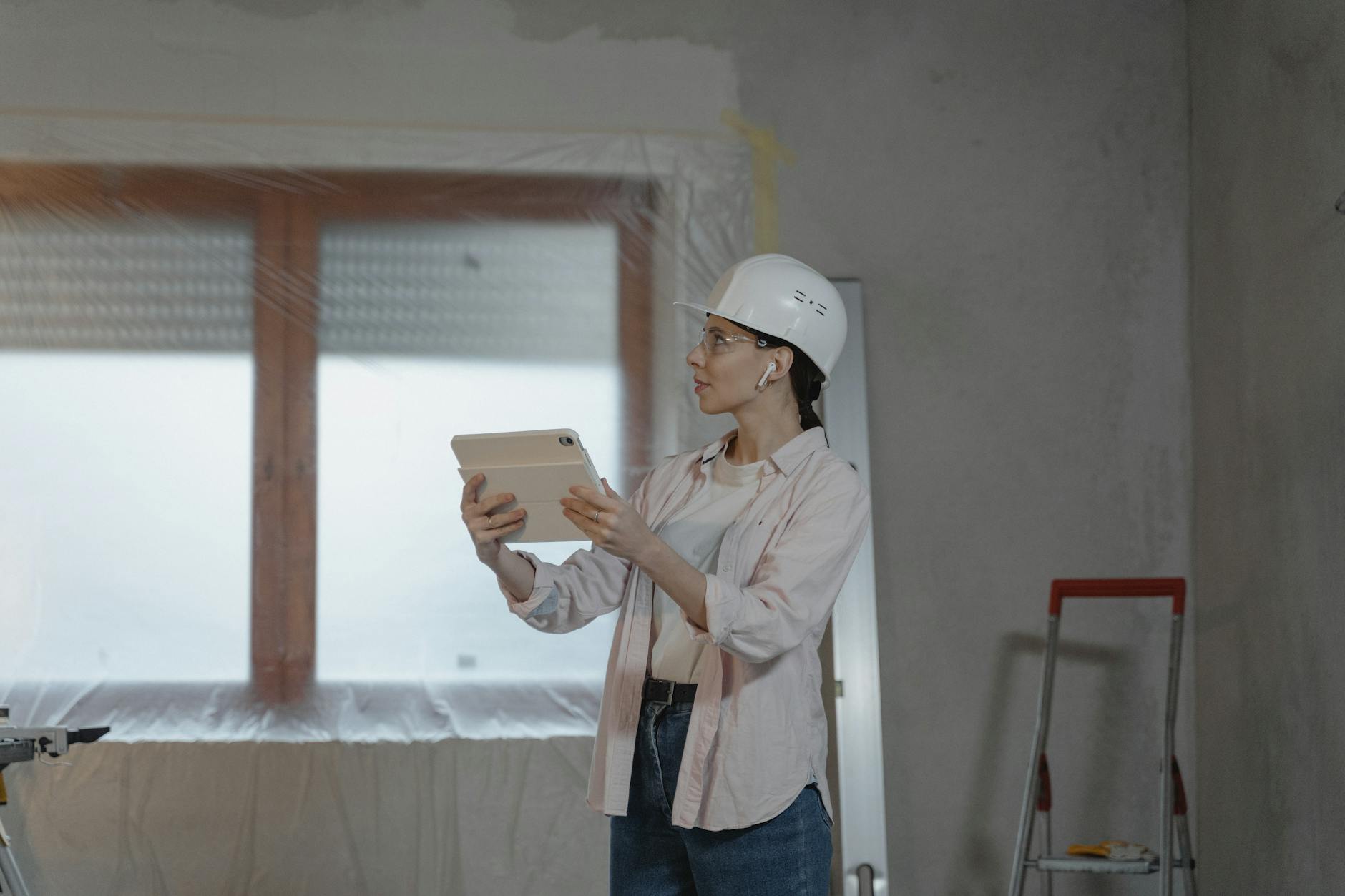 A female architect wearing a hard hat uses a tablet on a construction site for interior design planning. - renovation communication needs