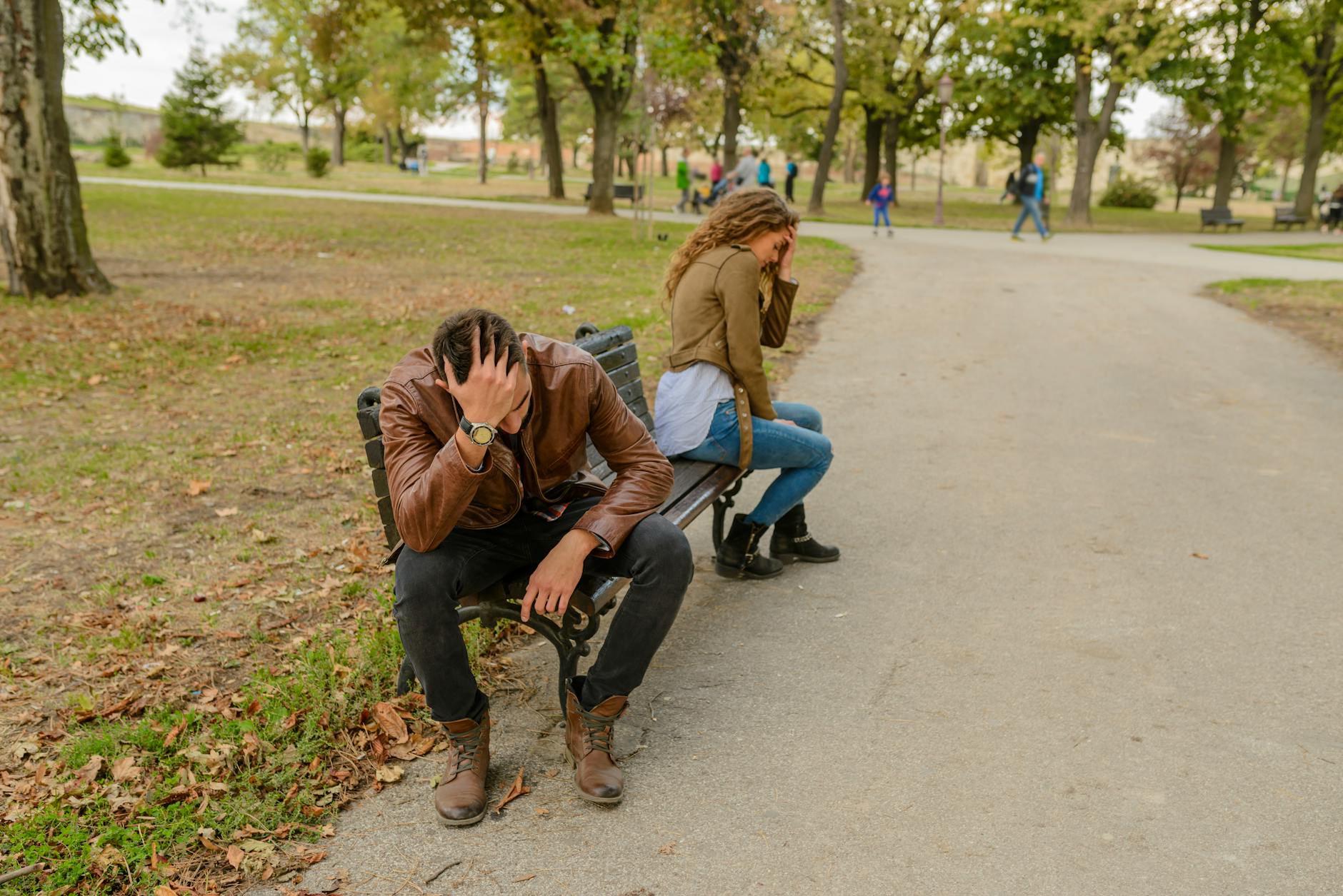 Distraught couple sitting apart on a park bench, facing away from each other, in a public park setting. - repairing trust after fight