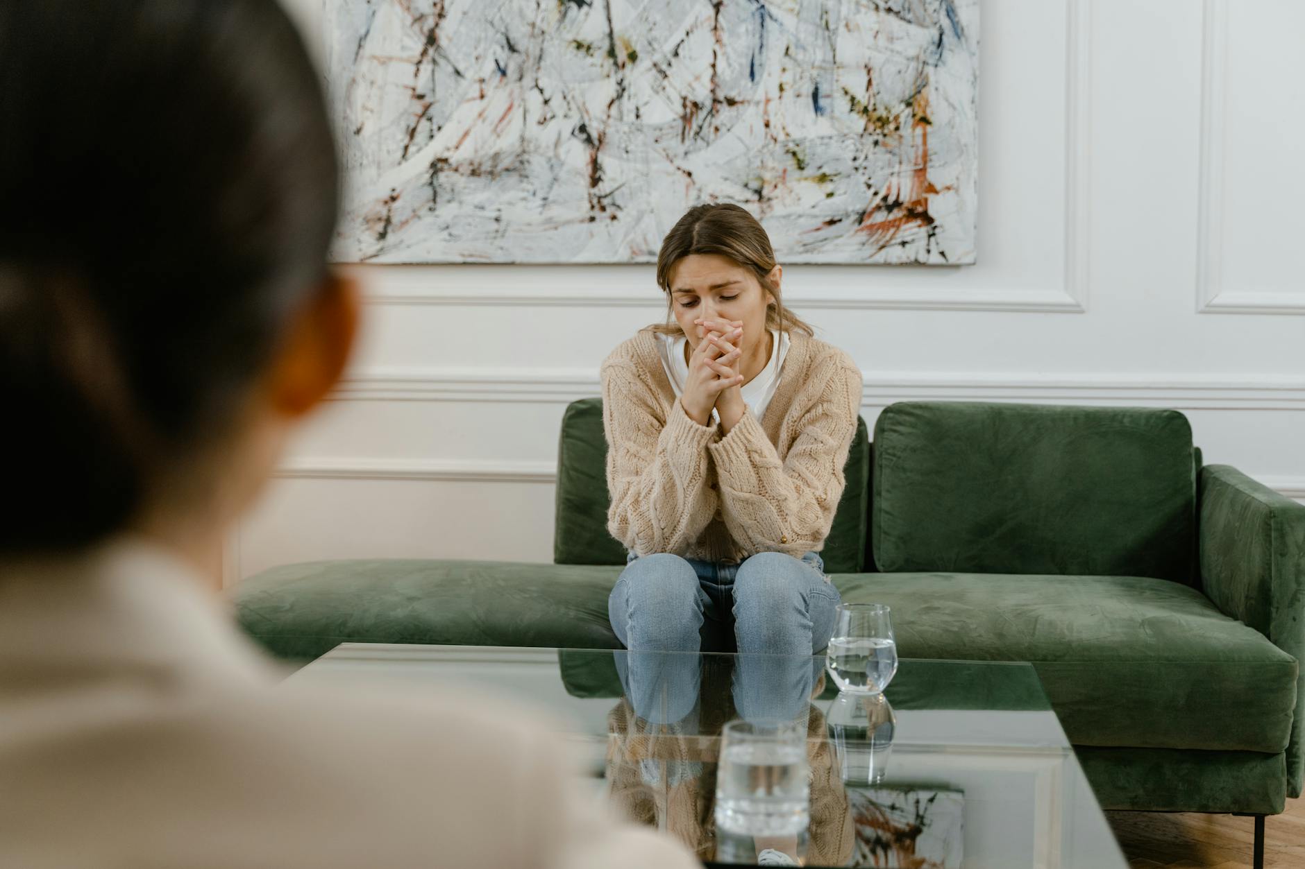 Woman in therapy session, seated on a green couch indoors, looking pensive. - sad therapist