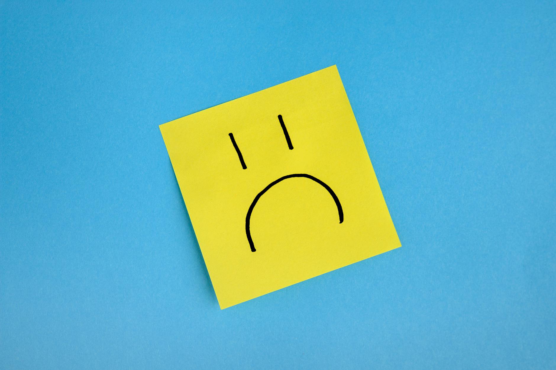 Yellow sticky note with sad face doodle on blue background, conveying emotions. - sad treatment options