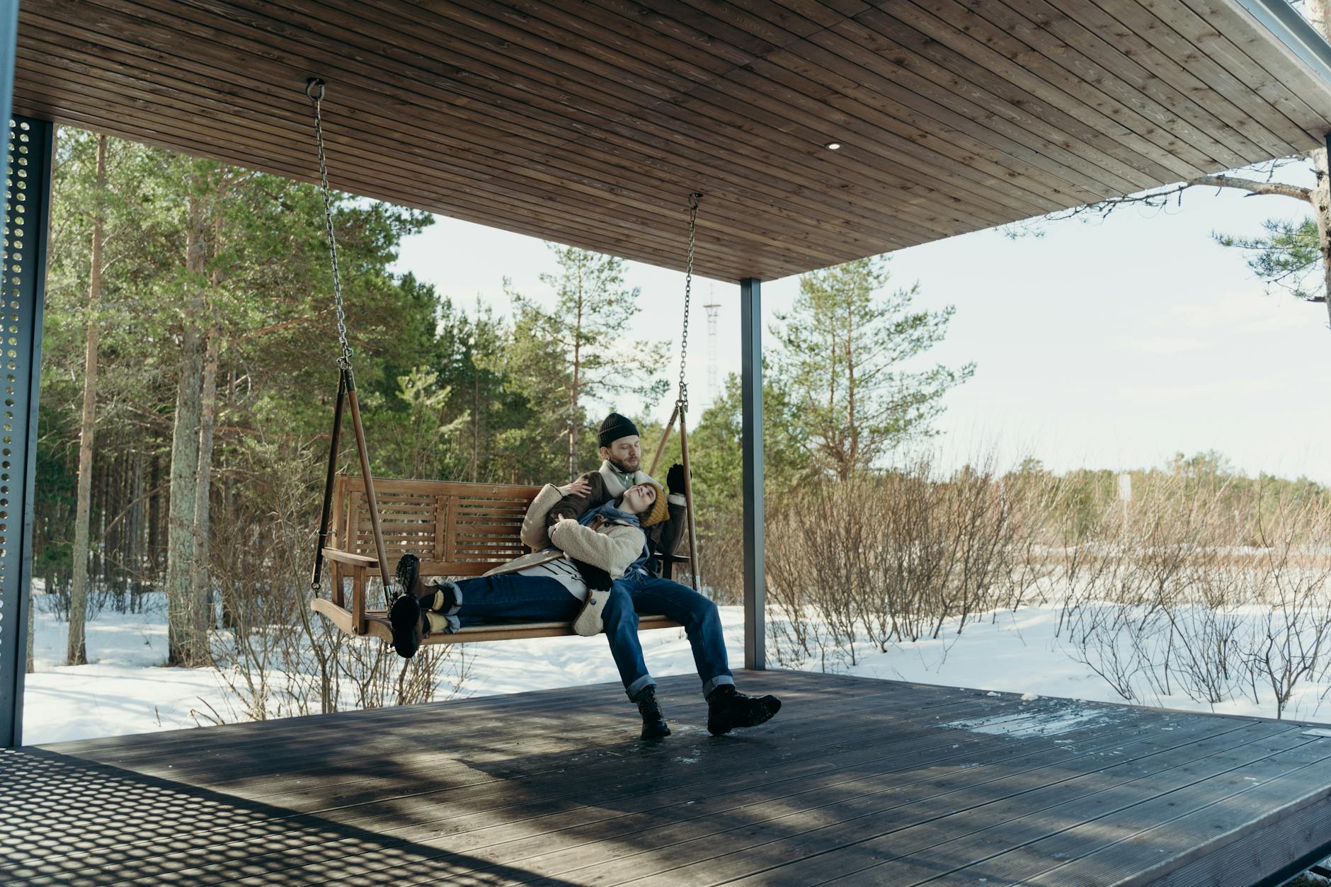 A couple enjoys a peaceful moment on a wooden swing amidst a snowy forest landscape. - seasonal mood swings